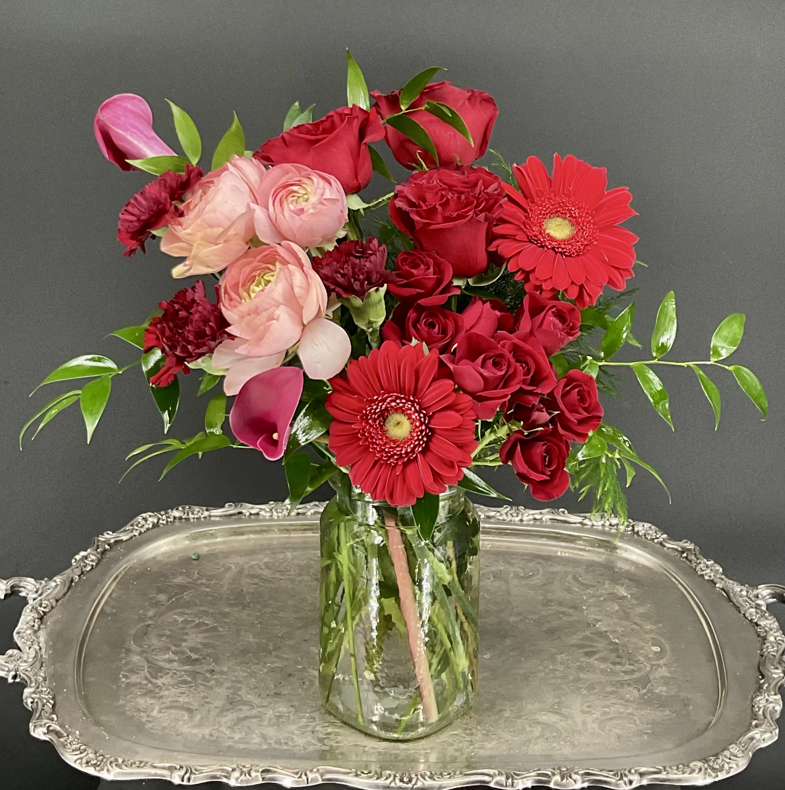 Colors of Love Bouquet - A lush blend of red roses, pink ranunculus, vibrant red gerbera daisies, and calla lilies, arranged with rich greenery in a timeless glass vase, symbolizing love, beauty, and devotion this Valentine's Day.