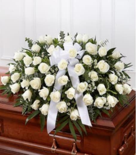 White Rose Half Casket Cover. - Our half casket cover, crafted with care and artistry by our expert florists with over 50 snow white roses, white monte casino, and accented with a white satin ribbon, is an unforgettable way to commemorate a lifetime of shared loving experiences.