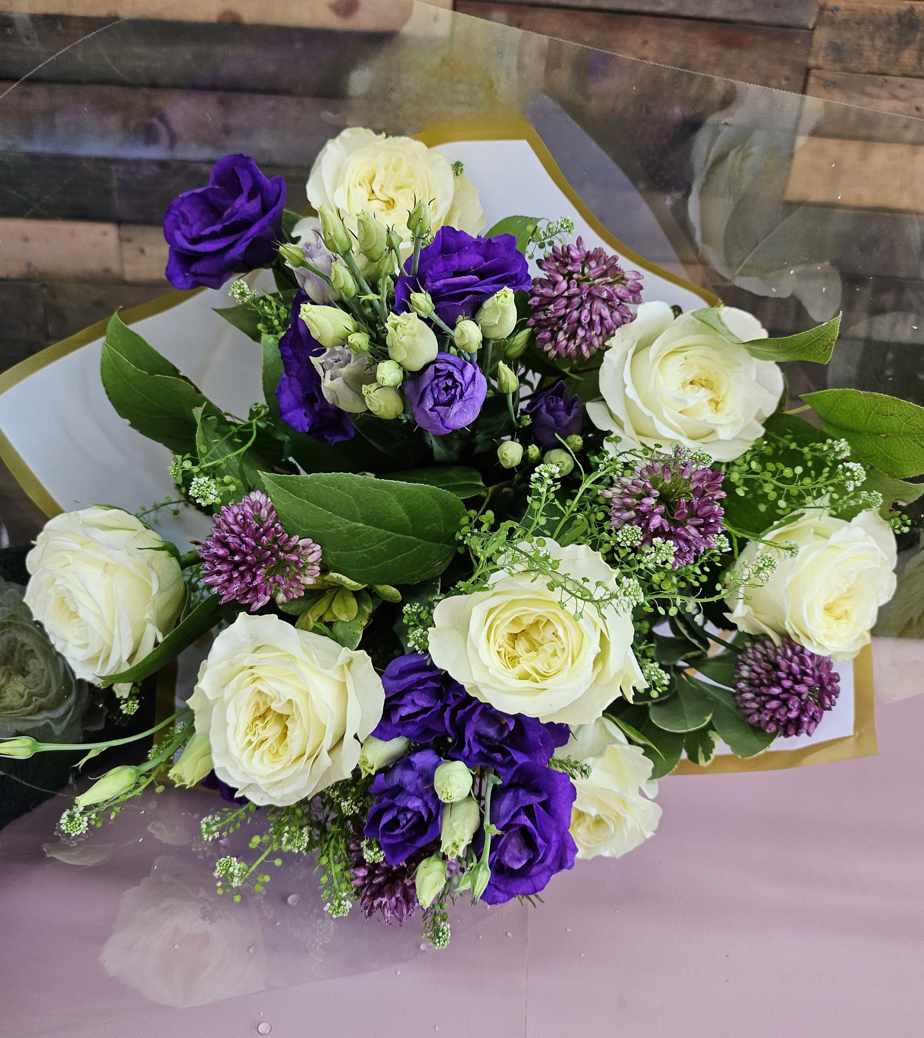 Elegant Purple and Cream Hand-Tied Bouquet - A vibrant mix of deep purple lisianthus, creamy white roses, and pops of textured purple accents come together to create this stunning hand-tied bouquet. Wrapped in premium, stylish paper, this bouquet exudes elegance and charm, perfect for any occasion.  Premium Flowers: White roses, purple lisianthus, and textured seasonal accents with lush greenery.  Wrapping: Finished in elegant wrapping paper to highlight the bouquet's vibrant colors.  Occasions: Ideal for birthdays, anniversaries, graduations, or simply as a thoughtful gesture to brighten someone's day.  Size: Approximately 12–16 inches in diameter, a generous size to make a bold impression.  Care Instructions: Trim stems and place in fresh water immediately upon receipt. Refresh water daily to maintain flower freshness.   This thoughtfully arranged bouquet is the perfect combination of vibrant colors and timeless beauty, guaranteed to make any occasion special.