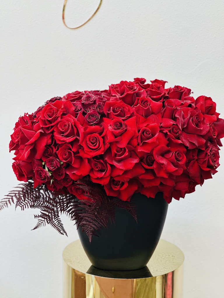 Red Reflection - Introducing **Red Reflection**, a striking floral arrangement that showcases the beauty of bold red roses, meticulously hand-designed by our talented team. Set in an elegant black vase, this captivating display creates a stunning contrast that enhances the vibrant hues of the roses. Each bloom is thoughtfully arranged to create a dynamic and eye-catching composition, making it a perfect centerpiece for any occasion. Whether celebrating a special moment or simply adding a touch of sophistication to your space, **Red Reflection** is a statement piece that exudes elegance and charm. Let this exquisite arrangement reflect your heartfelt sentiments and elevate your surroundings with its bold beauty.