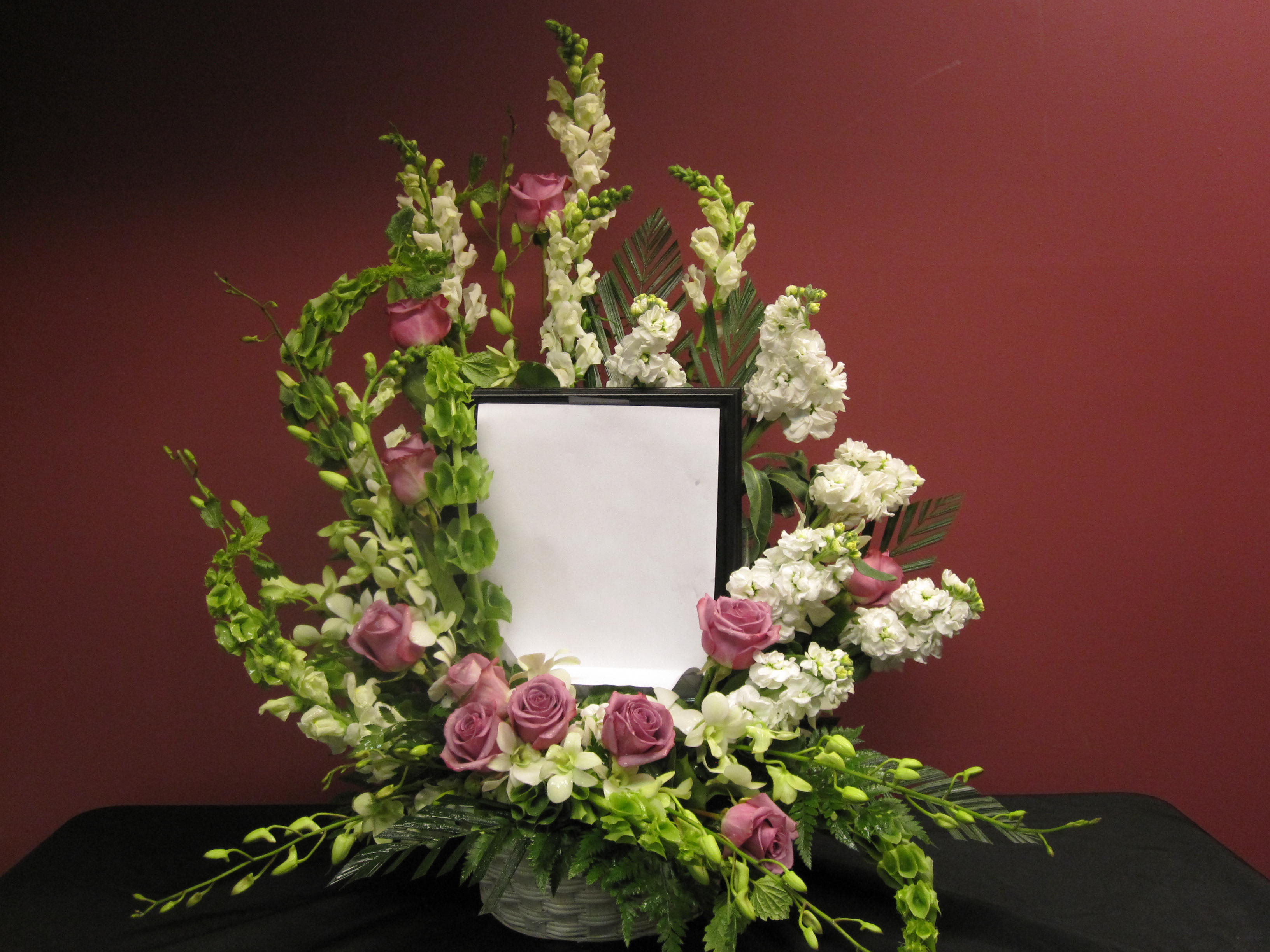 Loving Tribute Floral Frame - Lavenders roses, White stock, white snapdragons, white dendrobium orchids, and bells of Ireland lovingly frame an image of your dearly departed or a quote that is near and dear to your heart. Please note that we do not supply the frame or photo. 