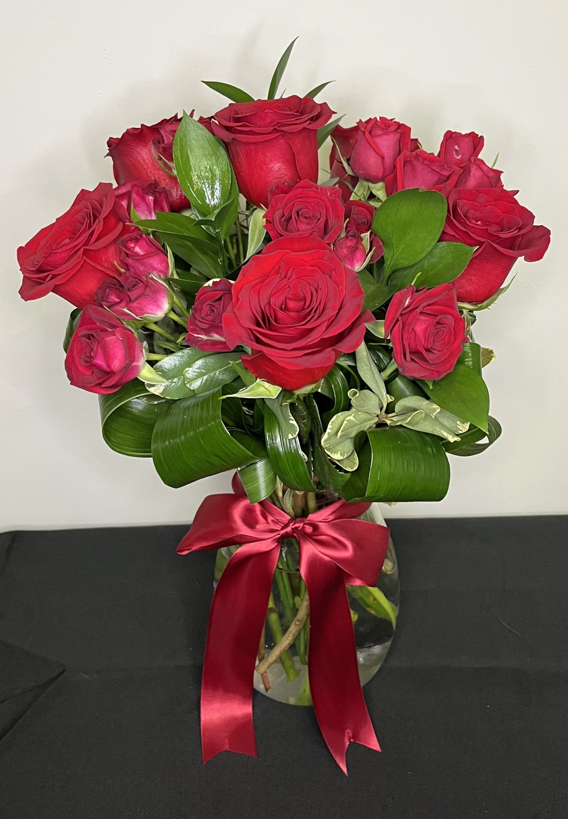 Love is in the Air by Chasing Petals - A stunning vase arrangement of rich red roses and red spray roses tied with an elegant red satin bow. 