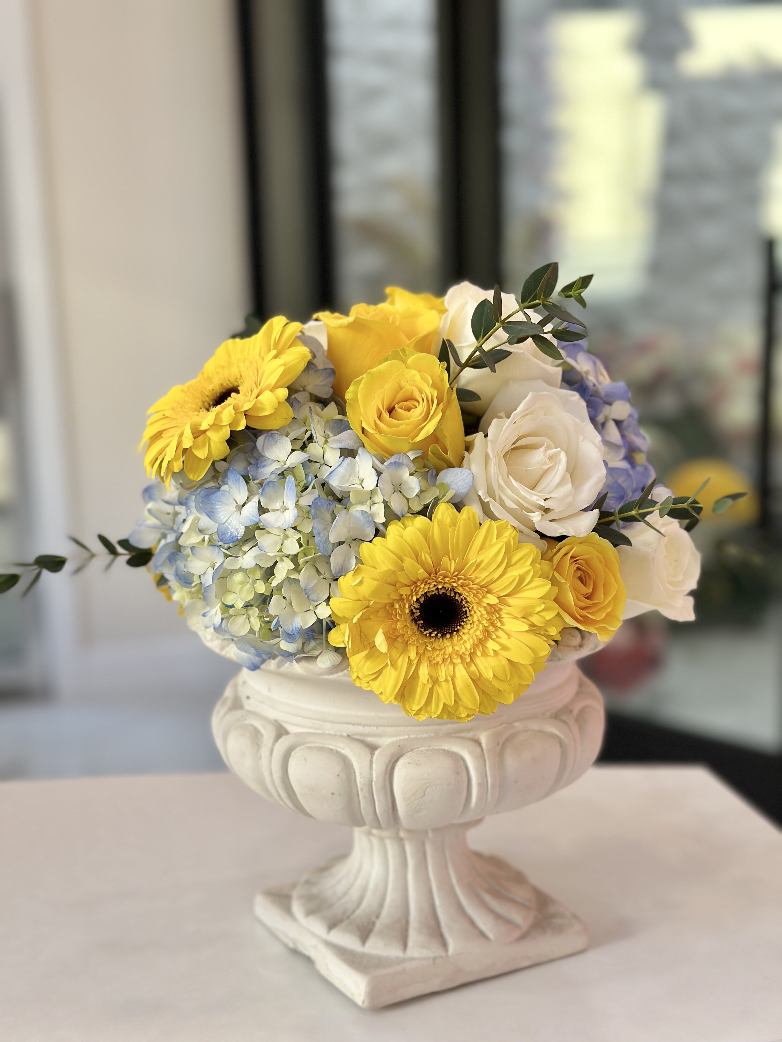 Sunny Garden Sunny Garden - An arrangement where the sunny yellow daisies and soft white roses join forces to bring an instant smile to your face. And just when you think it can't get any happier, in come the calming blue hydrangeas, like a breath of fresh air. This arrangement is all about spreading happiness and warmth, ready to brighten your loved one's day.