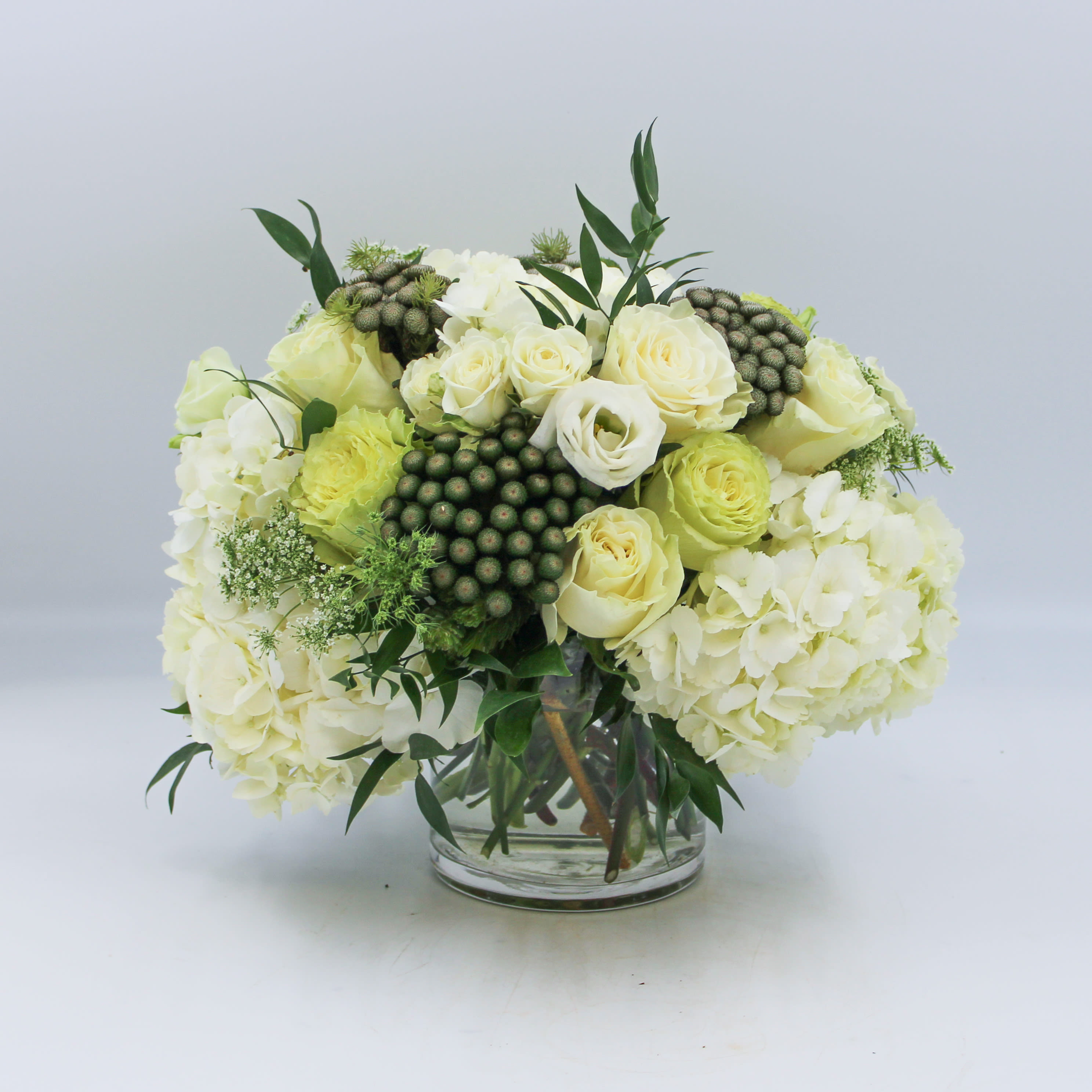 Dublin - Dublin is a luxurious display of White Hydrangea, Green Roses, White Roses, White Spray Roses, White Lisianthus, Green Brunia, Ruscus and Queen Anne’s Lace arranged in a clear glass cylinder. The Standard sized Dublin is arranged in a 5 inch cylinder and is pictured. The Deluxe and Premium sizes feature additional flowers in the same glass vase.