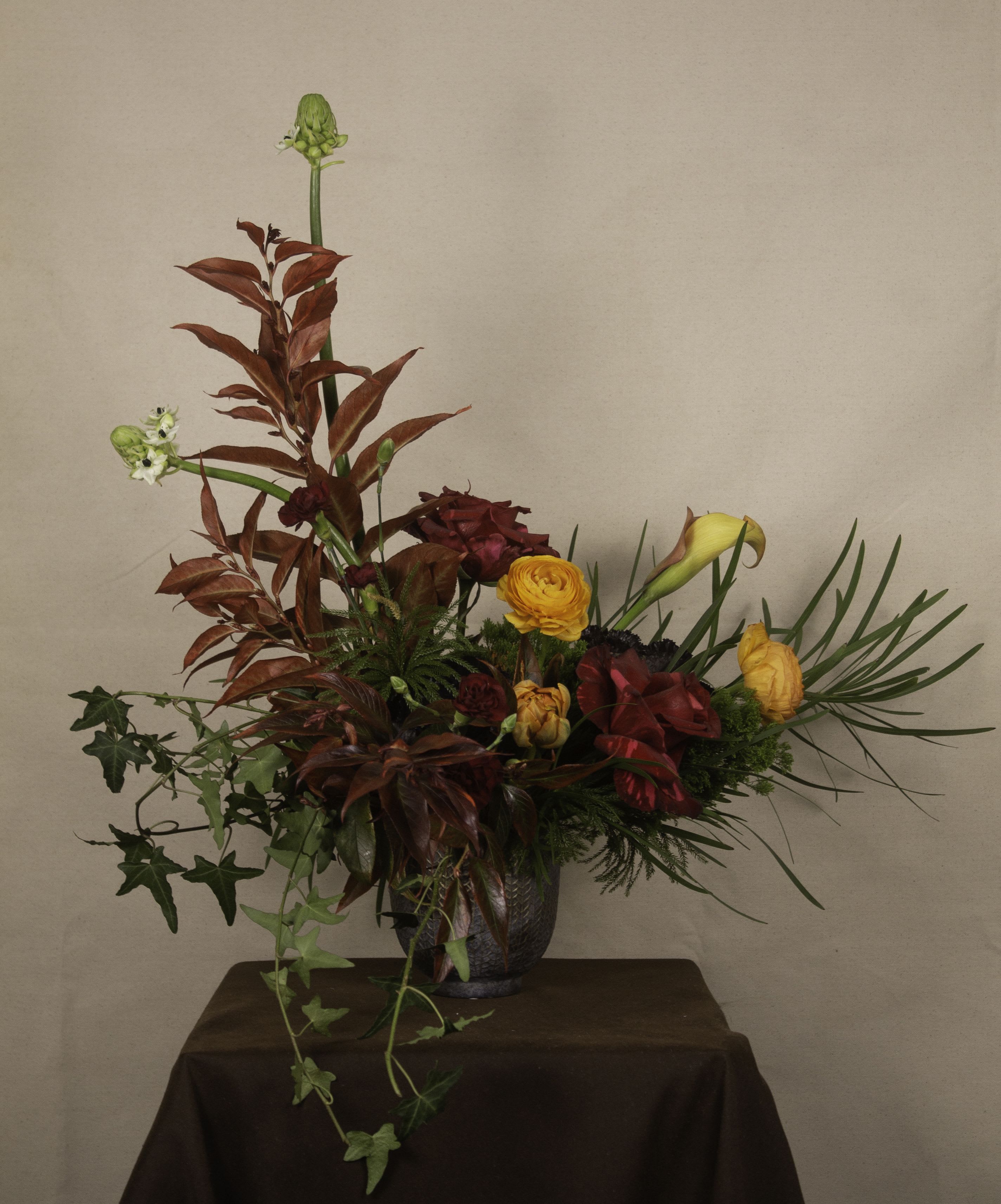 Rangoon - The Rangoon arrangement is a celebration of vibrant life and lush greenery, inspired by the bustling charm of its namesake city. Featuring fiery reds, deep oranges, and golden yellows balanced with rich foliage and cascading ivy, this design brings a sense of warmth and dynamic energy. Arranged in a textured vase, it evokes the beauty and vibrancy of Myanmar’s cultural heart. Perfect for adding a bold, artistic statement to any space.  ---------------------- At The Burmese Cat Floral Studio, we celebrate the uniqueness of every flower and vase. While the photo captures the spirit of your arrangement, some elements—like one-of-a-kind vessels or seasonal stems—might not always be exactly the same. However, each arrangement will embody the same charm, elegance, and artistic flair.  If substitutions are needed due to weather, seasonal shifts, or market availability, we’ll stay true to the mood, colors, and style you’ve chosen. Rest assured, any replacements will match or exceed the value of the original design.  If there’s something specific that’s a must-have for your arrangement, just let us know in the notes at checkout or reach out directly—we’ll do our best to make it happen! ----------------------