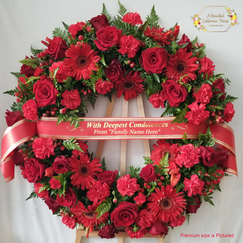 With Deepest Condolences - Red With Deepest Condolences - Red - Beautiful Memorial Wreath in Red. With roses, carnations, gerbera and red textural elements. Accented by lush greens. Comes displayed on wood easel, ready for the service. Customizable banner is additional $14.99, call for information. Wreath comes in two sizes as follows: Standard - 18 inch Wreath, approximate finnished size is 24" inches diameter Premium - 22" inch Wreath, approximate finnished size is 30" inches diameter (PICTURED) Wood Easel is 66" inches tall