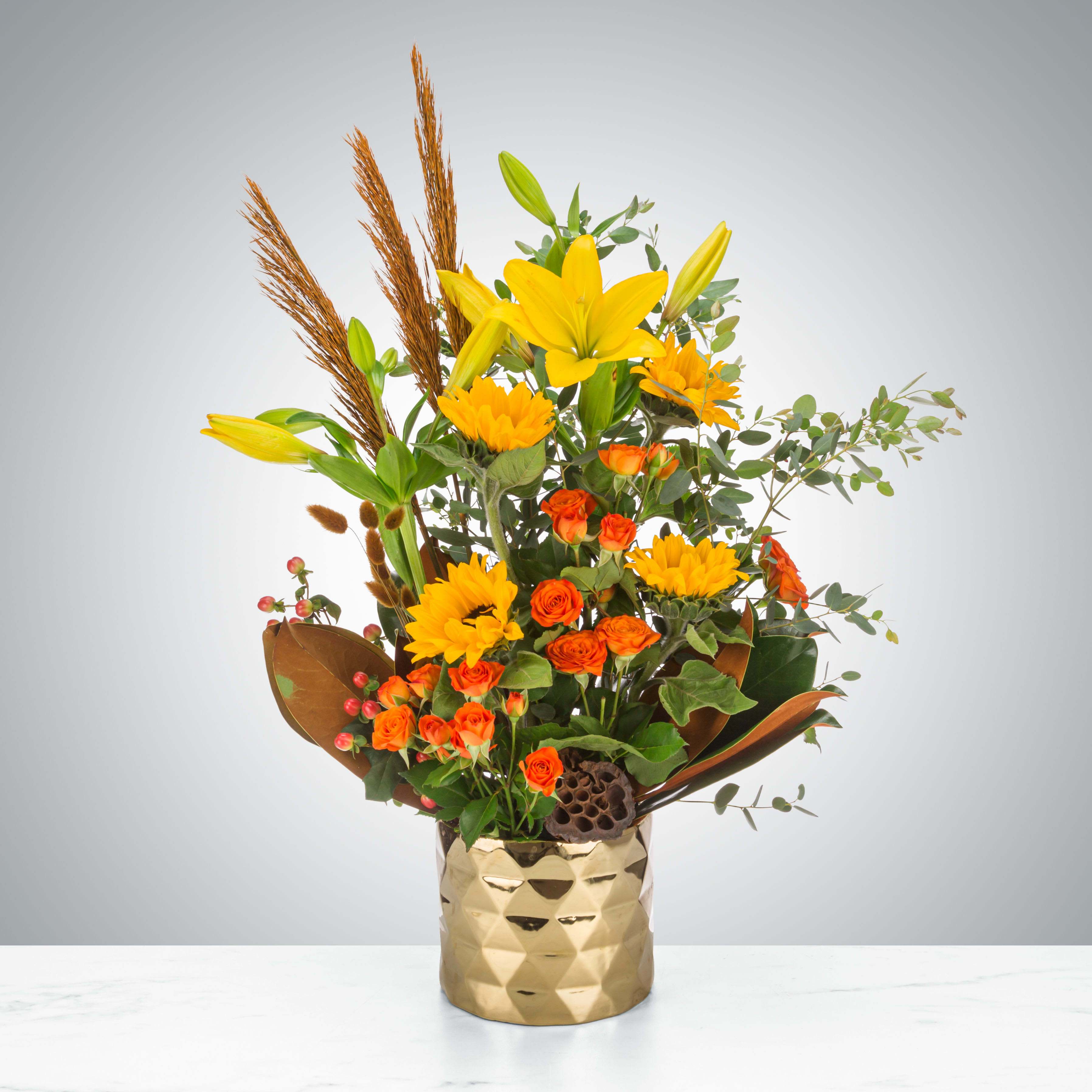 Autumn Glimmer by BloomNation™ Autumn Glimmer by BloomNation™ - Autumn glimmer is a quintessential fall arrangement featuring a gold architecture vase and a variety of fun fall flowers and accents. This arrangement is pure fun and elegance with a vase that the recipient will surely re-use. Send this to impress! Perfect for the autumn equinox, Halloween or Thanksgiving. Approximate Dimensions: 16"D x 25"H