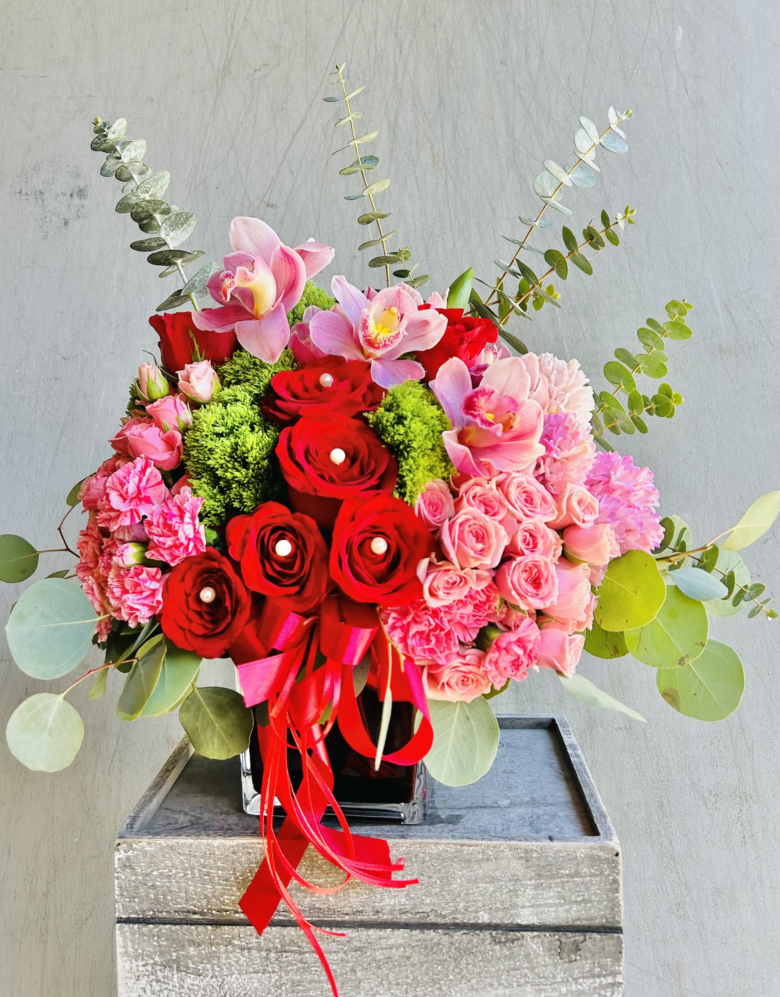 Cupid's Cheer - Beautiful red and pink arrangement featuring red roses, pink spray roses, orchids, carnations, and green accents. 