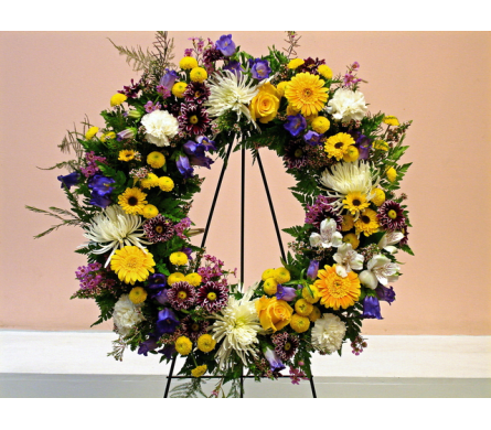 Aurora Wreath - W156 - Decorate an important ceremony with Fillmore Florist's standing Aurora Wreath. This stunning standing wreath is made with Spider Chrysanthemum yellow Buttons Roses Gerbera Daisy purple Camapnulla white Carnations and a verity of fillers and greens. This arrangement comes with a five foot tall easel which the wreath hangs from.Dimensions Approximately: 24&quot; H x 24&quot; W As Shown : W156
