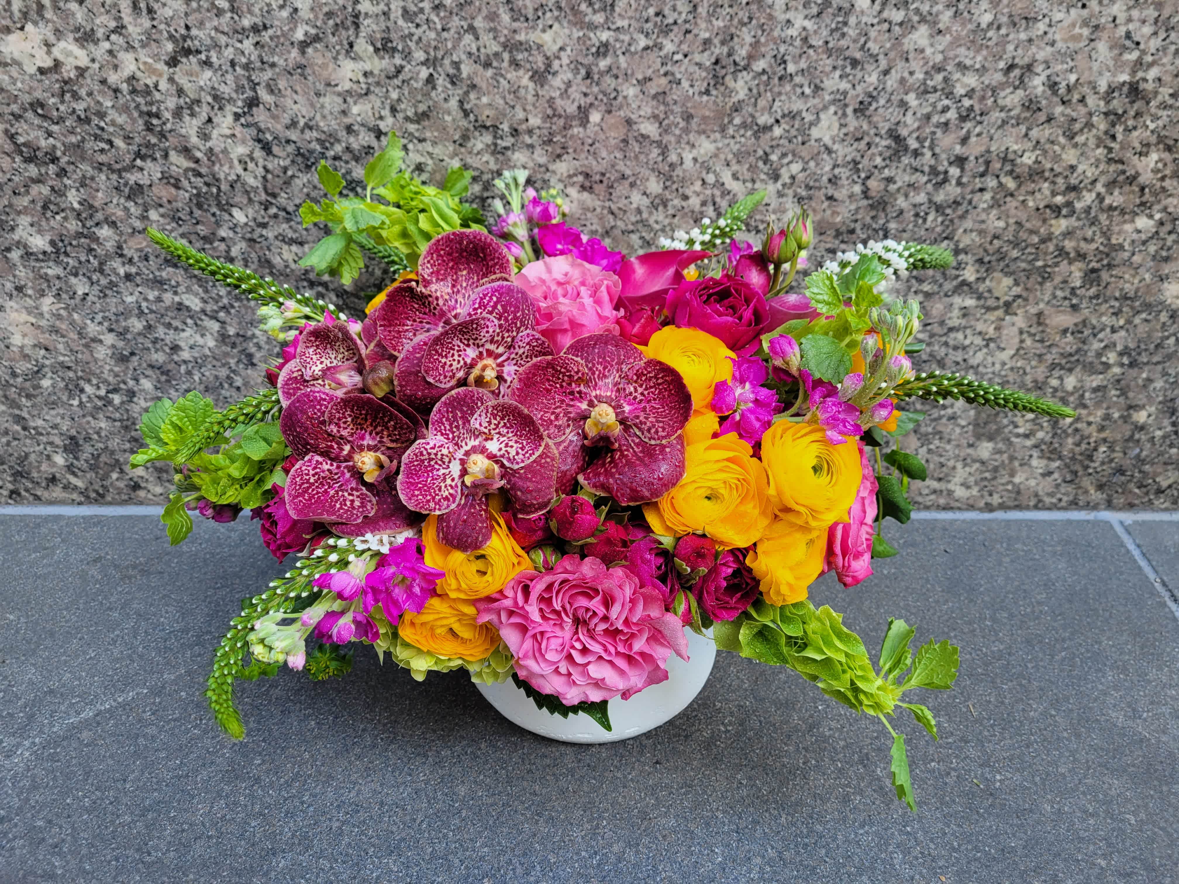 Scarlet Sunset - Immerse yourself in the brilliance of our Scarlet Sunset arrangement, where vibrant red vanda orchids, sunny yellow roses, and soft pink blooms unite in a captivating display. Each bloom sings its own melody, creating a dynamic composition that mirrors the warmth and vibrancy of a tropical sunset. Perfect for adding a burst of color and energy to any setting, this arrangement is a harmonious celebration of nature's beauty and the joy it brings.