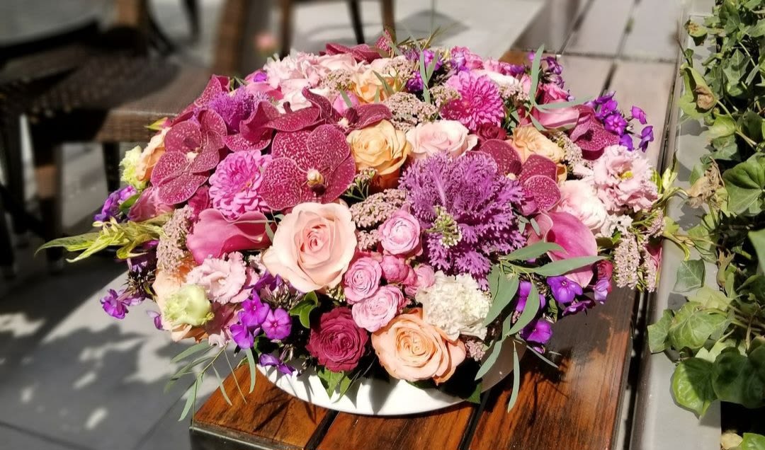 Powder Pink - This stunning arrangement showcases a harmonious blend of powder pink and autumn hues, creating a warm and inviting display. Lush orchids, with their graceful petals, are beautifully paired with soft pink roses, adding a touch of romance and sophistication. Accented with seasonal foliage and hints of warm gold, this composition evokes the essence of fall while celebrating the beauty of blooming flowers. Perfect for any occasion, this arrangement brings a serene and elegant touch to your space, embodying the beauty of the changing seasons.