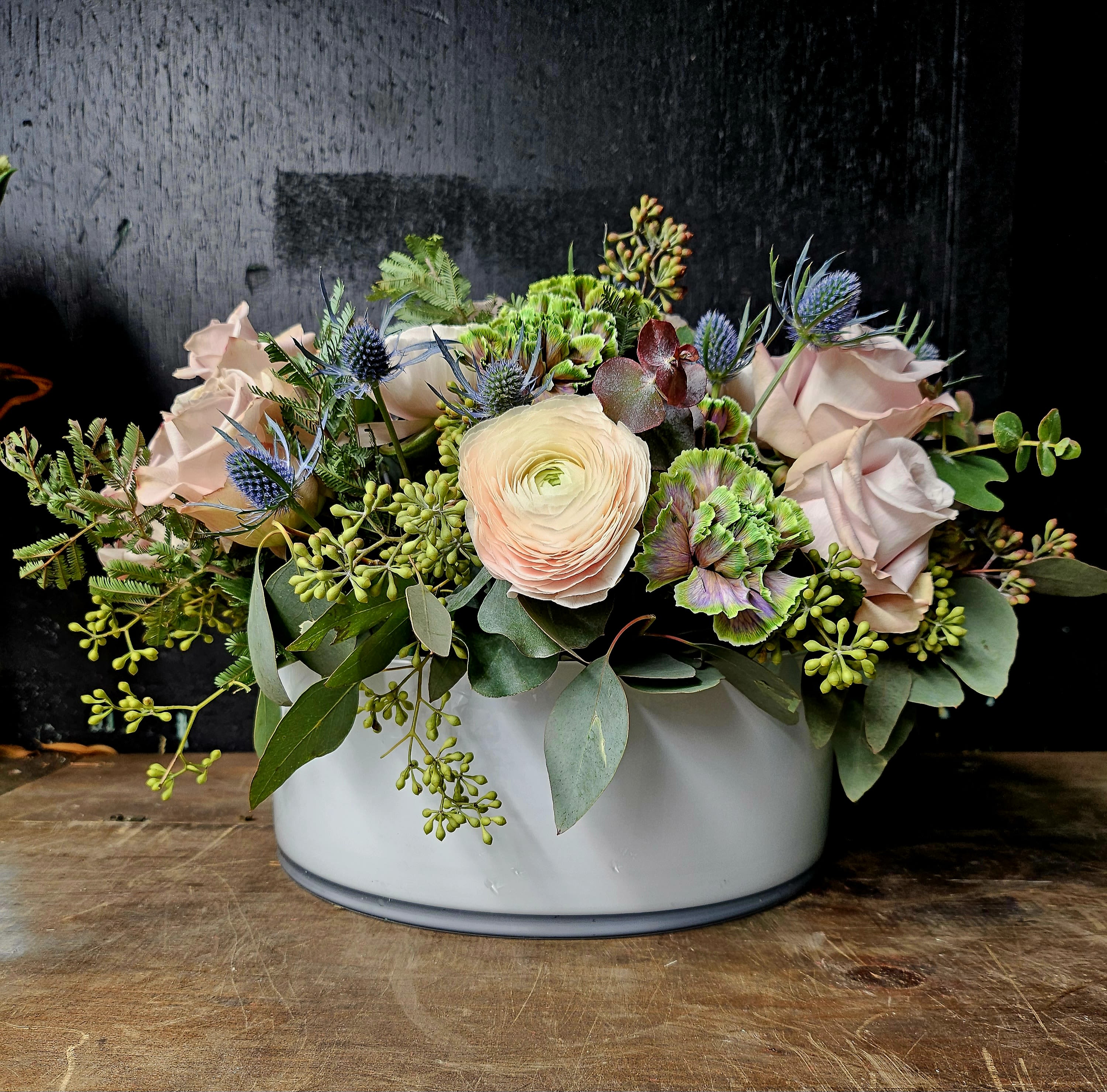 Lush Green Hydrangea &amp; Ranunculus Elegance Arrangement - Immerse yourself in the beauty of our luxurious floral arrangement featuring hydrangeas, ranunculus, thistle, eucalyptus, and delicate antique roses. This masterpiece showcases a harmonious blend of soft greens, creams, and muted blush tones, complemented by textured greenery that evokes a sense of natural elegance. Designed in a chic white ceramic vase, this arrangement is perfect for adding a touch of sophistication to any occasion.  Premium Flowers: Handpicked hydrangeas, ranunculus, thistle, antique roses, and lush eucalyptus.  Occasion: Ideal for weddings, anniversaries, housewarmings, or as a stunning centerpiece.  Bring this lush and timeless arrangement into your home or gift it to a loved one to create unforgettable memories.