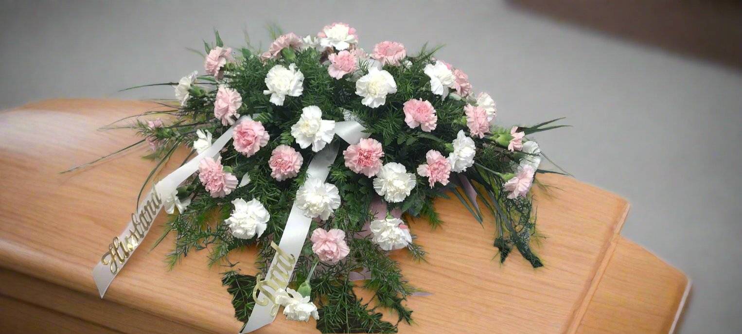 Comforting Carnations Casket Saddle - Express your deepest sympathies with our Comforting Carnations casket saddle, a beautifully arranged tribute that honors cherished memories. These elegant sympathy flowers are designed to provide peace and comfort during difficult times, making them the ideal choice to show your love and support.  Each floral spray is meticulously crafted by our skilled florists to reflect the essence of your loved one, ensuring a unique piece that resonates with your vision. Trust us to deliver a heartfelt floral tribute that not only honors their memory but also brings solace to all who gather to celebrate their life.