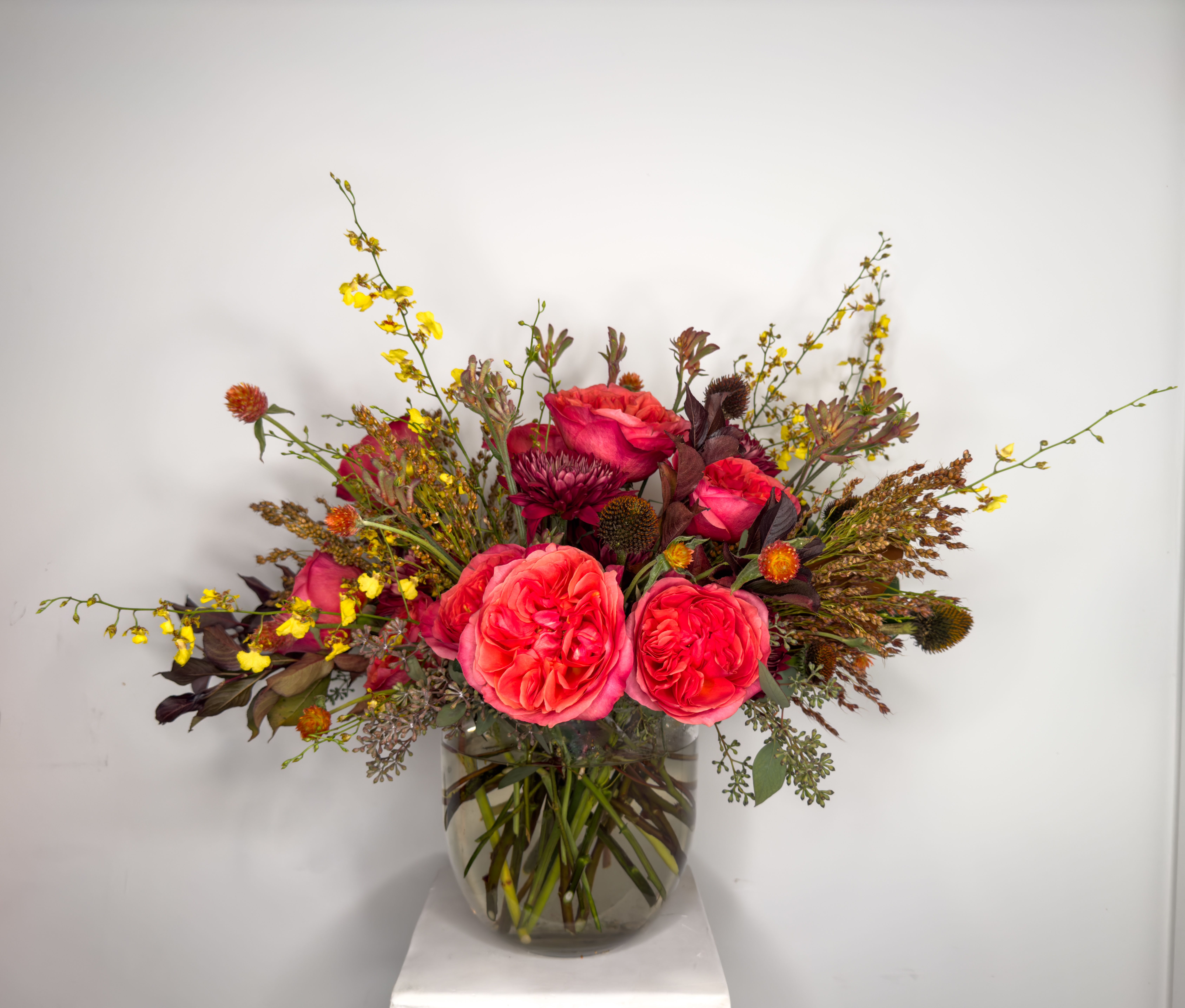 Timeless Elegance Timeless Elegance - Embrace the beauty of autumn with our Timeless Elegance Bouquet, a sophisticated floral arrangement that captures the season's rich hues. This round design, styled in a modern cylinder with a rounded bottom, features a stunning array of darker autumn tones, including deep hot pinks and rich rusts, creating a striking contrast. Longer tendrils of oncidium orchids gracefully cascade from the sides, adding an artistic flair and enhancing the bouquet's dimension. Perfect for elevating your décor or as a thoughtful gift, this arrangement embodies both tradition and modernity, making it a captivating focal point in any space. APPROXIMATE DIMENSIONS ARE 20" W X 20" H