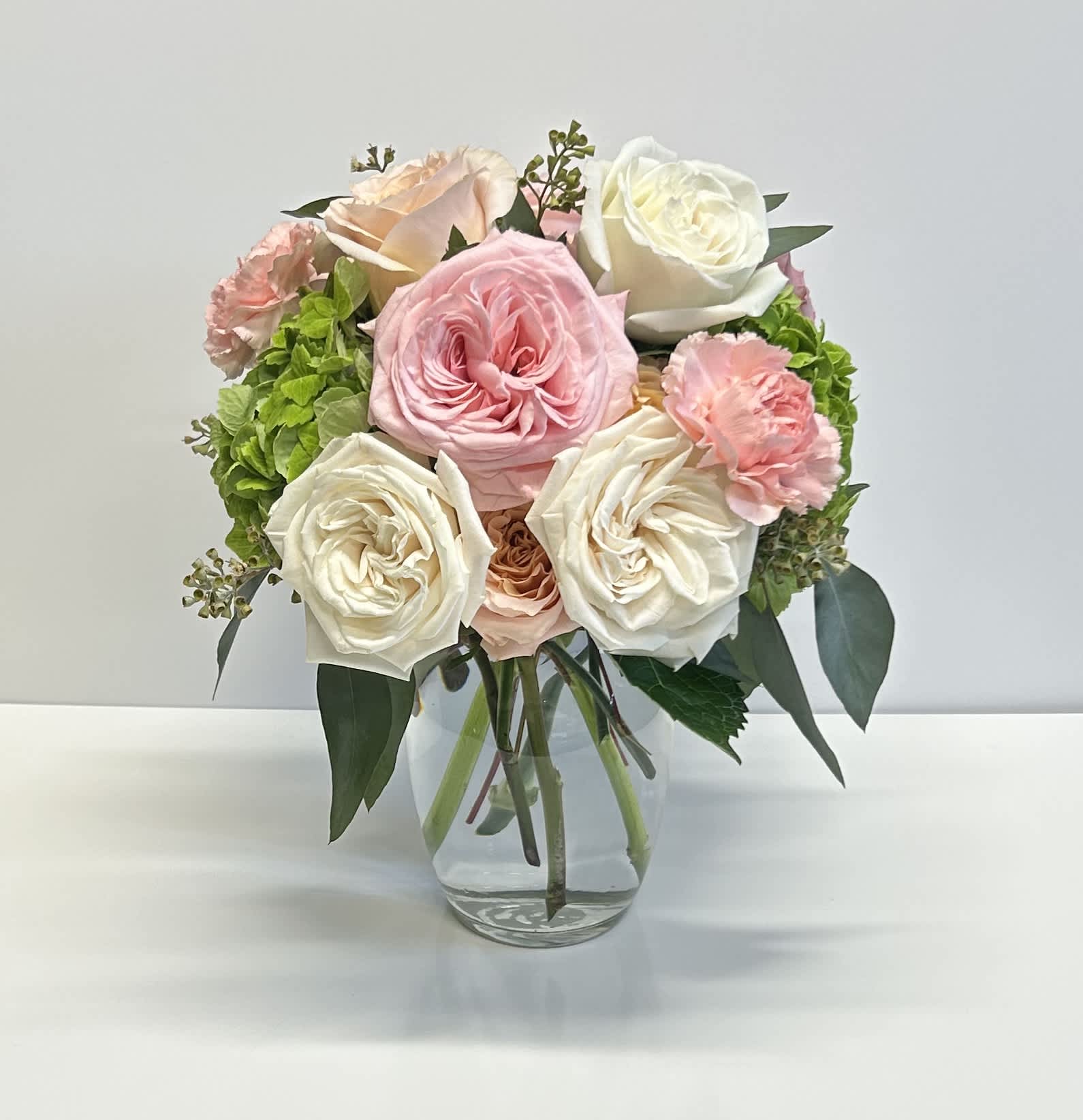 Simi - For this classic we have playa blanca garden roses, pink o'hara garden roses, shimmer roses, pink carnations, green hydrangea and a touch of seeded eucalyptus designed into a classic ginger vase. This arrangement is slightly fragrant. 