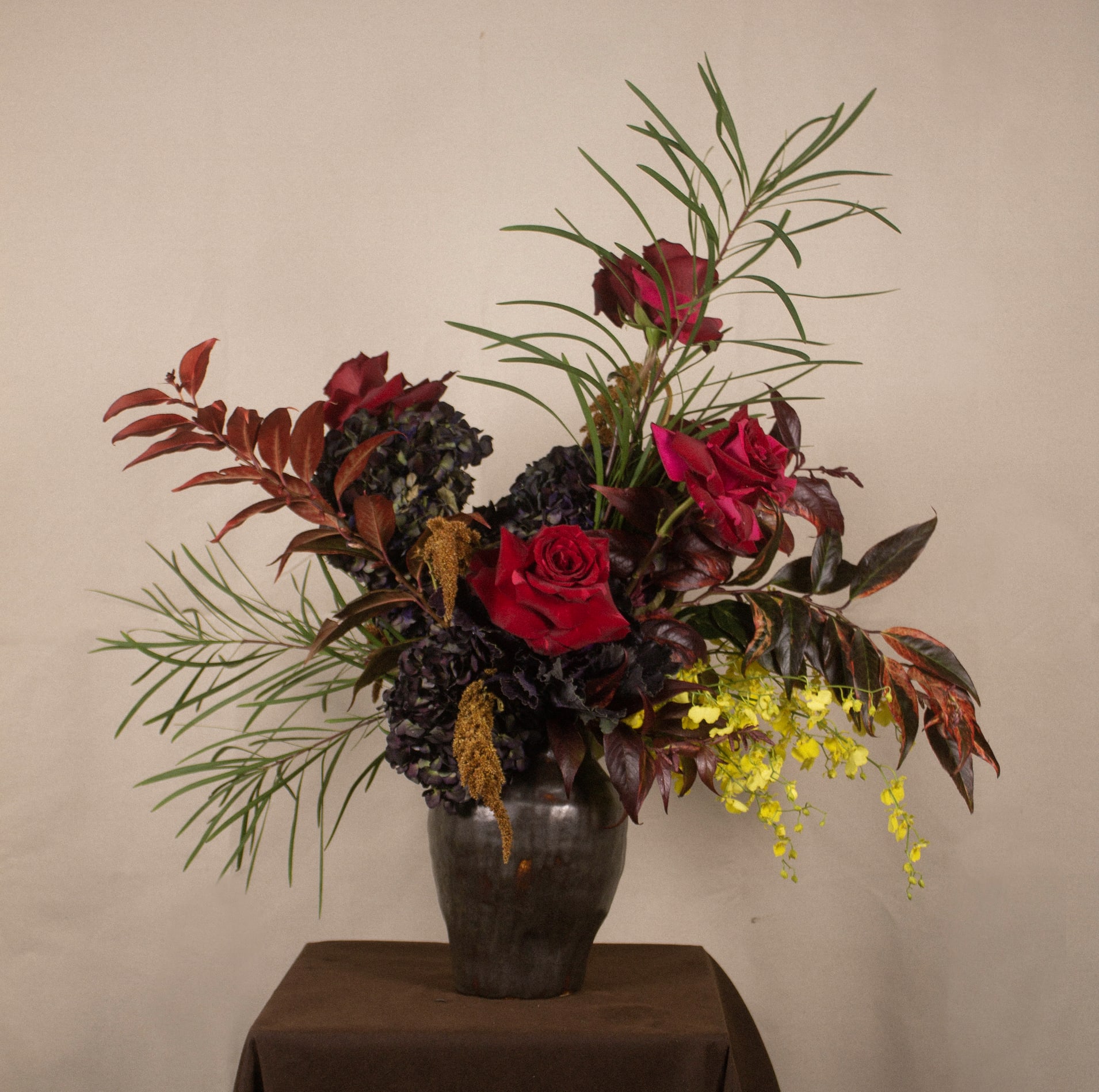 Mandalay - The &quot;Mandalay&quot; floral arrangement draws inspiration from the city of Mandalay, capturing its rich cultural and natural beauty. This striking composition features deep red roses and textured dark hydrangeas, symbolizing the city's timeless elegance. Cascading golden amaranthus adds a graceful touch, while vibrant yellow orchids introduce a lively pop of color. Framed by soft greenery and reddish foliage, the arrangement exudes dynamic, organic energy. Presented in a rustic dark vase, it evokes the sophistication and dramatic charm of Mandalay, making a bold and memorable statement.  --------------------------------- At The Burmese Cat Floral Studio, we celebrate the uniqueness of every flower and vase. While the photo captures the spirit of your arrangement, some elements—like one-of-a-kind vessels or seasonal stems—might not always be exactly the same. However, each arrangement will embody the same charm, elegance, and artistic flair.  If substitutions are needed due to weather, seasonal shifts, or market availability, we’ll stay true to the mood, colors, and style you’ve chosen. Rest assured, any replacements will match or exceed the value of the original design.  If there’s something specific that’s a must-have for your arrangement, just let us know in the notes at checkout or reach out directly—we’ll do our best to make it happen! ---------------------------------