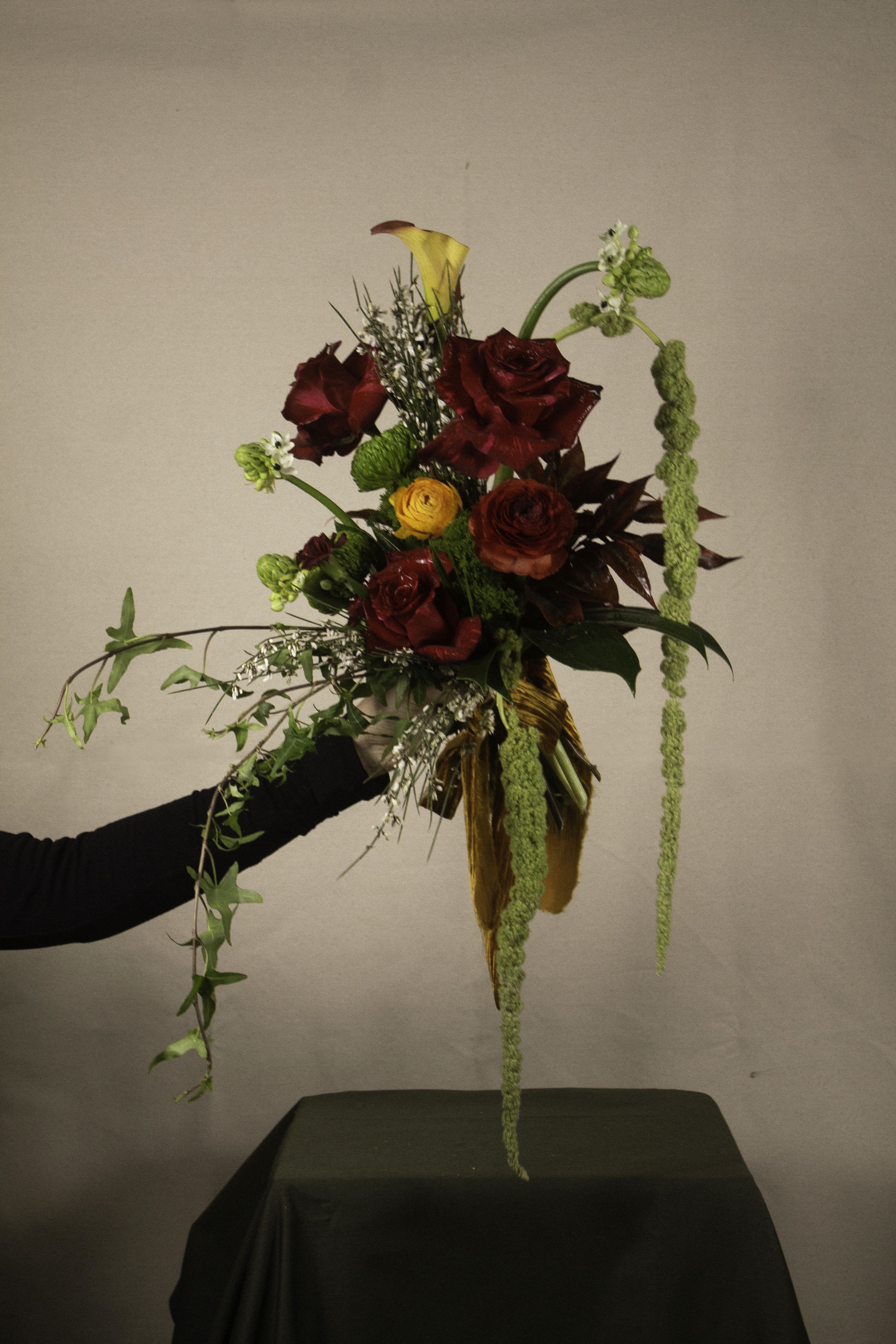 The Burmese Cat Signature Bouquet - A bold and dramatic composition, The Burmese Cat bouquet blends deep crimson roses with striking golden accents, playful textures, and cascading greenery. Designed with a sense of movement and mystery, it’s tied together with a velvet ribbon, exuding elegance and allure. Perfect for those who appreciate a touch of drama and timeless beauty.  ---------------------- At The Burmese Cat Floral Studio, we celebrate the uniqueness of every flower and vase. While the photo captures the spirit of your arrangement, some elements—like one-of-a-kind vessels or seasonal stems—might not always be exactly the same. However, each arrangement will embody the same charm, elegance, and artistic flair.  If substitutions are needed due to weather, seasonal shifts, or market availability, we’ll stay true to the mood, colors, and style you’ve chosen. Rest assured, any replacements will match or exceed the value of the original design.  If there’s something specific that’s a must-have for your arrangement, just let us know in the notes at checkout or reach out directly—we’ll do our best to make it happen! ----------------------