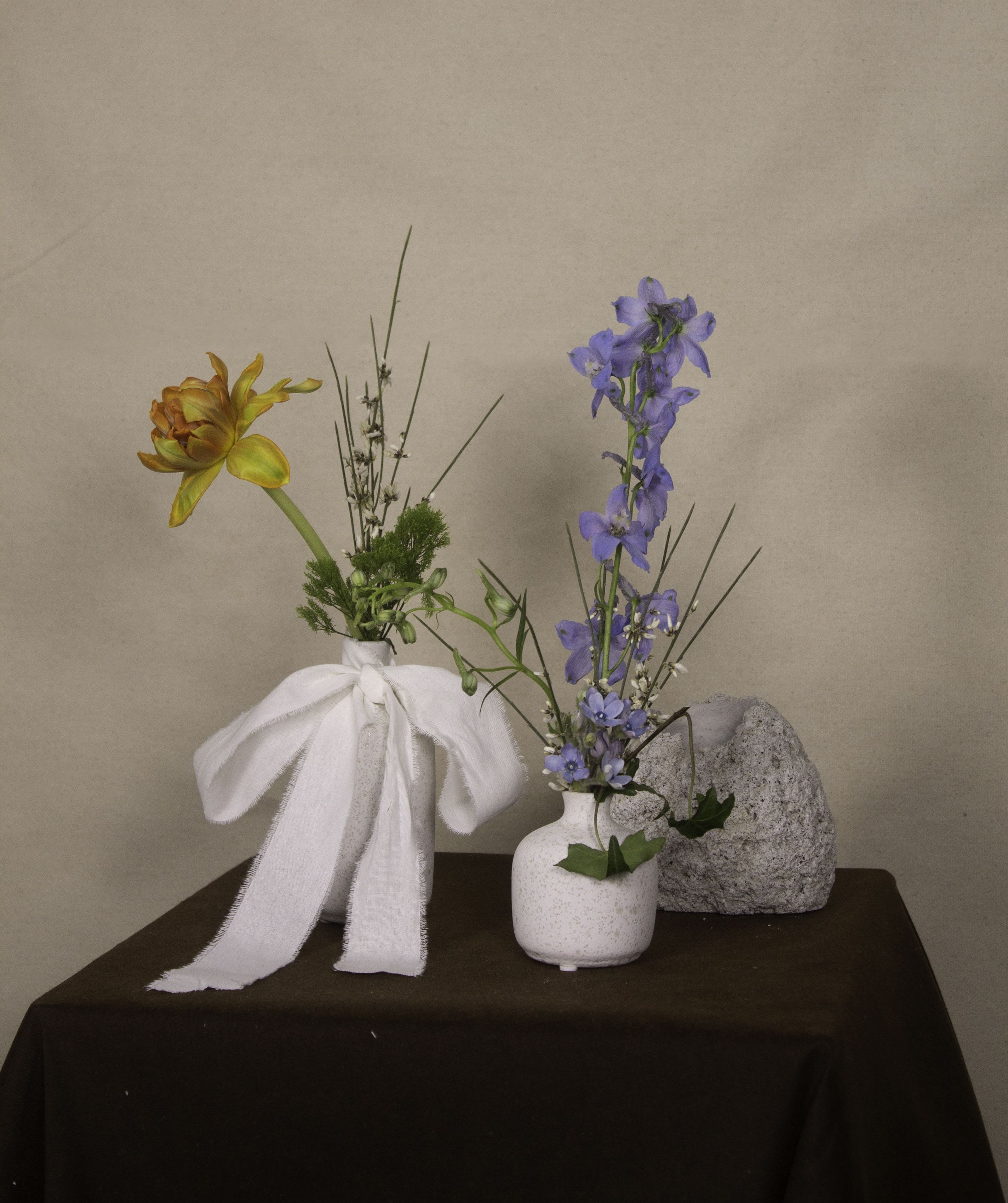 Karaweik Twins - The &quot;Karaweik Twins&quot; is a set of two delicate bud vases inspired by the elegance and symmetry of the iconic Karaweik palace.The first vase features a vibrant orange tulip, green dill sprigs, and slender twigs. The second showcases blue delphiniums, white wax flowers, ivy, and airy grass stems, creating a harmonious blend of colors and textures.  Crafted with textured ceramic, each vase showcases a unique shape, complementing one another beautifully. Paired with minimalistic floral arrangements, the set evokes a serene and timeless aesthetic, making it a graceful addition to any home or workspace. ---------------------------------------------------  At The Burmese Cat Floral Studio, we celebrate the uniqueness of every flower and vase. While the photo captures the spirit of your arrangement, some elements—like one-of-a-kind vessels or seasonal stems—might not always be exactly the same. However, each arrangement will embody the same charm, elegance, and artistic flair.  If substitutions are needed due to weather, seasonal shifts, or market availability, we’ll stay true to the mood, colors, and style you’ve chosen. Rest assured, any replacements will match or exceed the value of the original design.  If there’s something specific that’s a must-have for your arrangement, just let us know in the notes at checkout or reach out directly—we’ll do our best to make it happen!