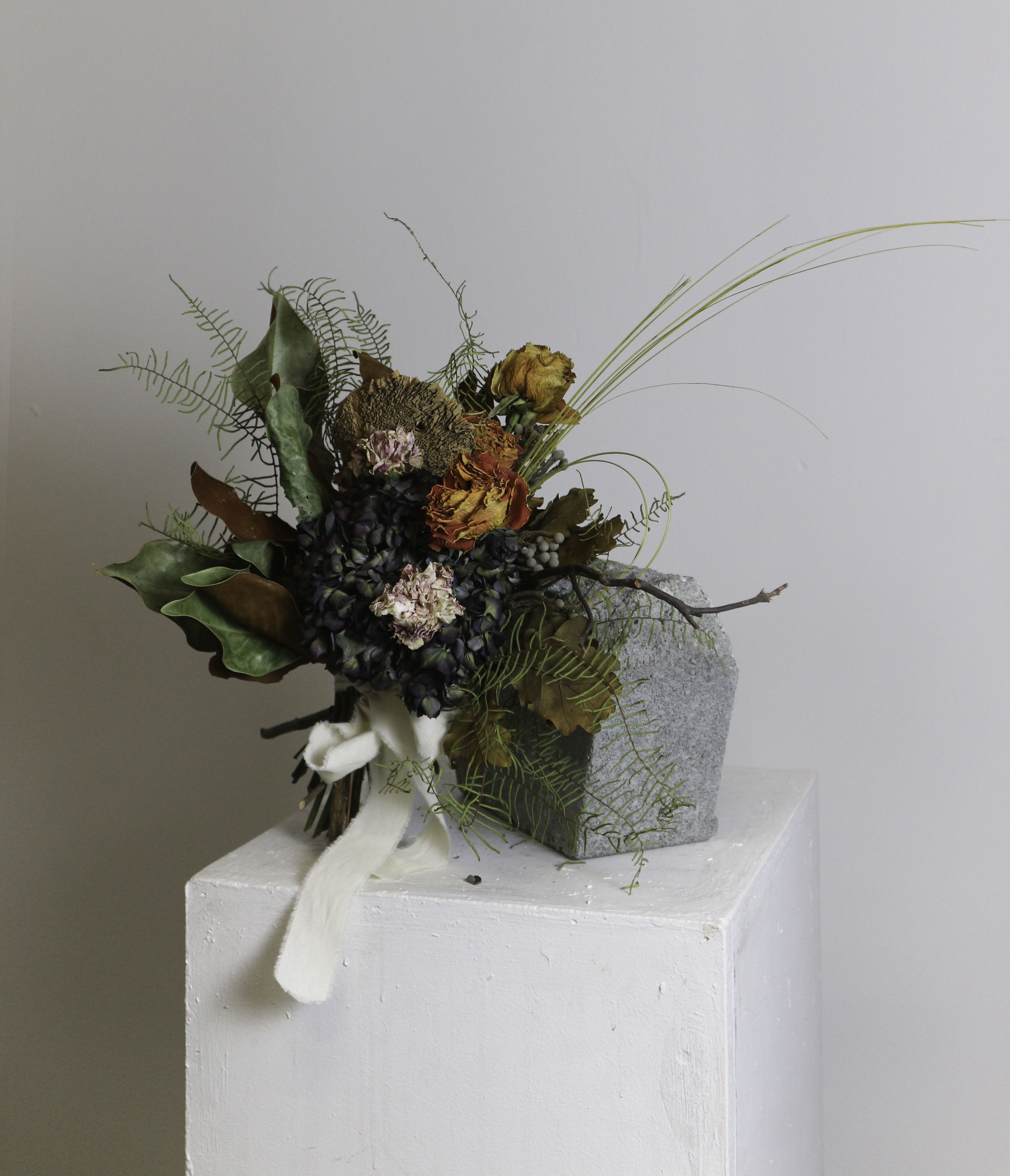 Thida (Dried Bouquet) - Thida is a captivating bouquet blending dried and preserved elements for a timeless and rustic aesthetic. With deep, muted hues of purple and orange, complemented by rich greens and earthy tones, it features textured accents like ferns, hydrangeas, and aged foliage. This organic arrangement is bound with a soft, flowing ribbon, evoking elegance and natural beauty.  ---------------------------------------------------  At The Burmese Cat Floral Studio, we celebrate the uniqueness of every flower and vase. While the photo captures the spirit of your arrangement, some elements—like one-of-a-kind vessels or seasonal stems—might not always be exactly the same. However, each arrangement will embody the same charm, elegance, and artistic flair.  If substitutions are needed due to weather, seasonal shifts, or market availability, we’ll stay true to the mood, colors, and style you’ve chosen. Rest assured, any replacements will match or exceed the value of the original design.  If there’s something specific that’s a must-have for your arrangement, just let us know in the notes at checkout or reach out directly—we’ll do our best to make it happen!