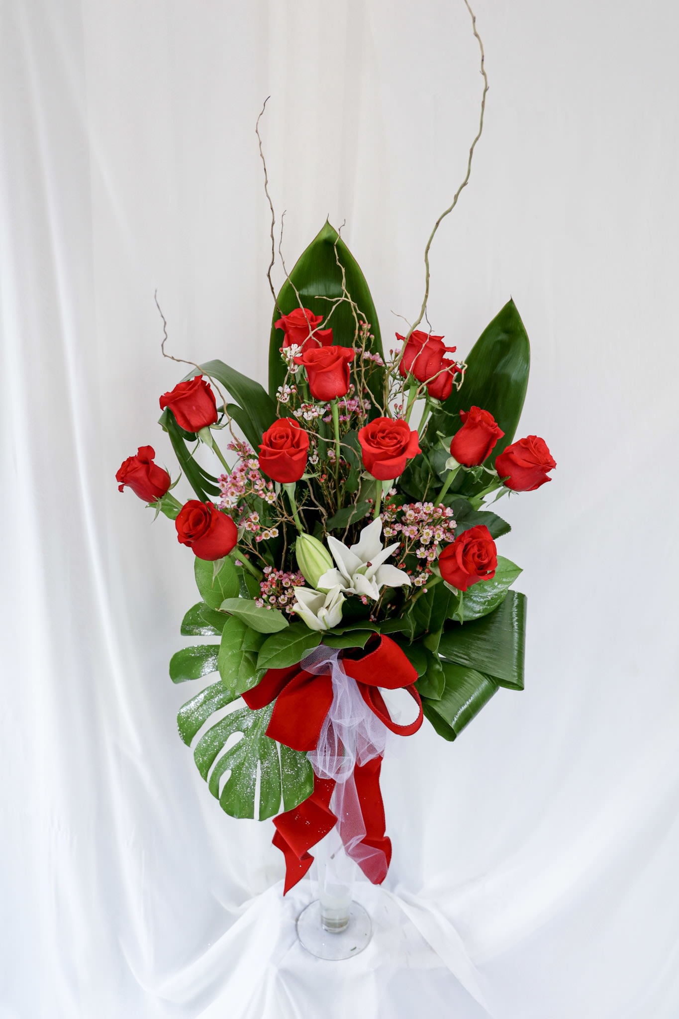 Cupid's Love Cupid's Love - This arrangement consists of one dozens roses along with lilies and is topped of with beautiful tropical leaves. It is an excellent arrangmnet to give for an anniversary, special occasion or just because.