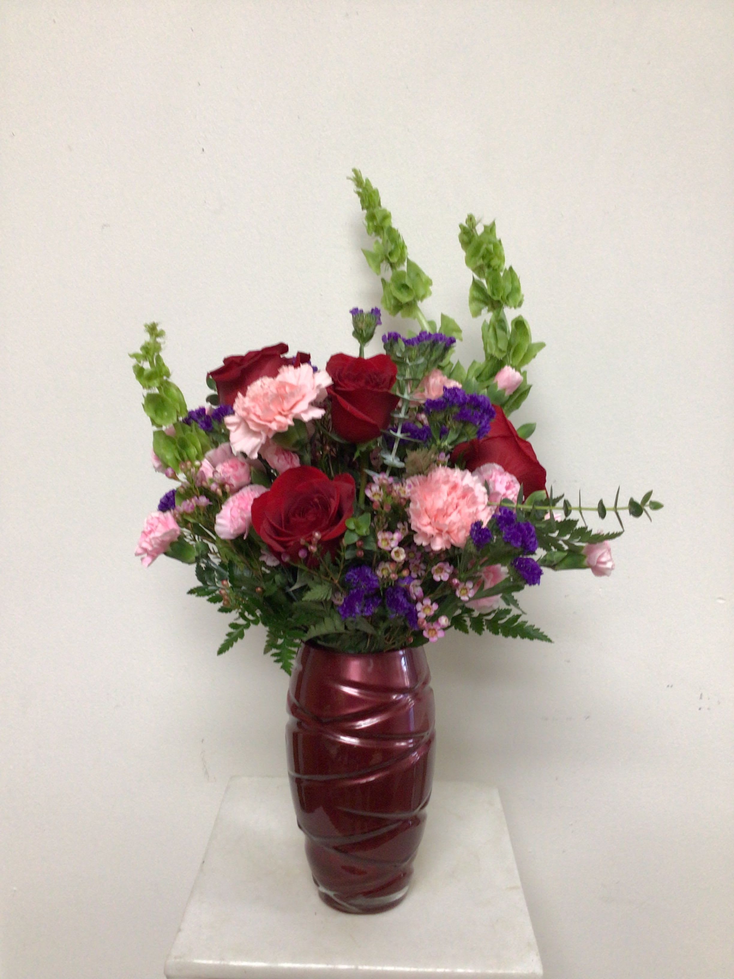Deep red swirl - Red swirl vase is arranged red roses, pink carnations, pink miniature carnations, purple statice, bells of Ireland, lavender waxflower and assorted greenery. Approximate size is 11 inches wide by 23 inches tall.