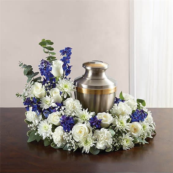 Cremation Wreath-Blue And White - &quot;Honor a life so beautifully lived. Our florists artistically hand-design an asymmetrical blue and white table wreath arrangement with roses, carnations, delphinium and more. An urn or framed photograph can be placed in the open center, creating a comforting tribute for the cremation or memorial service. • Our florists hand-design each arrangement, so colors and varieties may vary due to local availability • Asymmetrical arrangement of blue delphinium and white roses, carnations, cushion poms and football mums; accented with spiral and seeded eucalyptus, gypsophila and variegated pittosporum • Send to the cremation service or memorial service; urn or framed photograph can be placed in the center