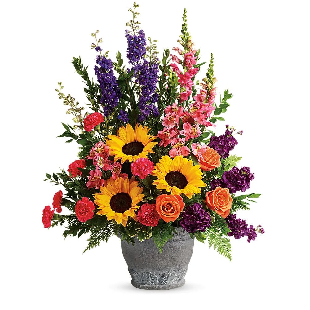 Hues Of Hope Bouquet - Send a message of warmth and hope with this magnificent display of sunflowers and roses in a large antiqued pot, a colorful tribute that will warm their hearts. This bright arrangement includes orange roses, pink alstroemeria, hot pink carnations, yellow sunflowers, purple larkspur, purple stock, hot pink snapdragons, myrtle, variegated pittosporum, and leatherleaf fern.