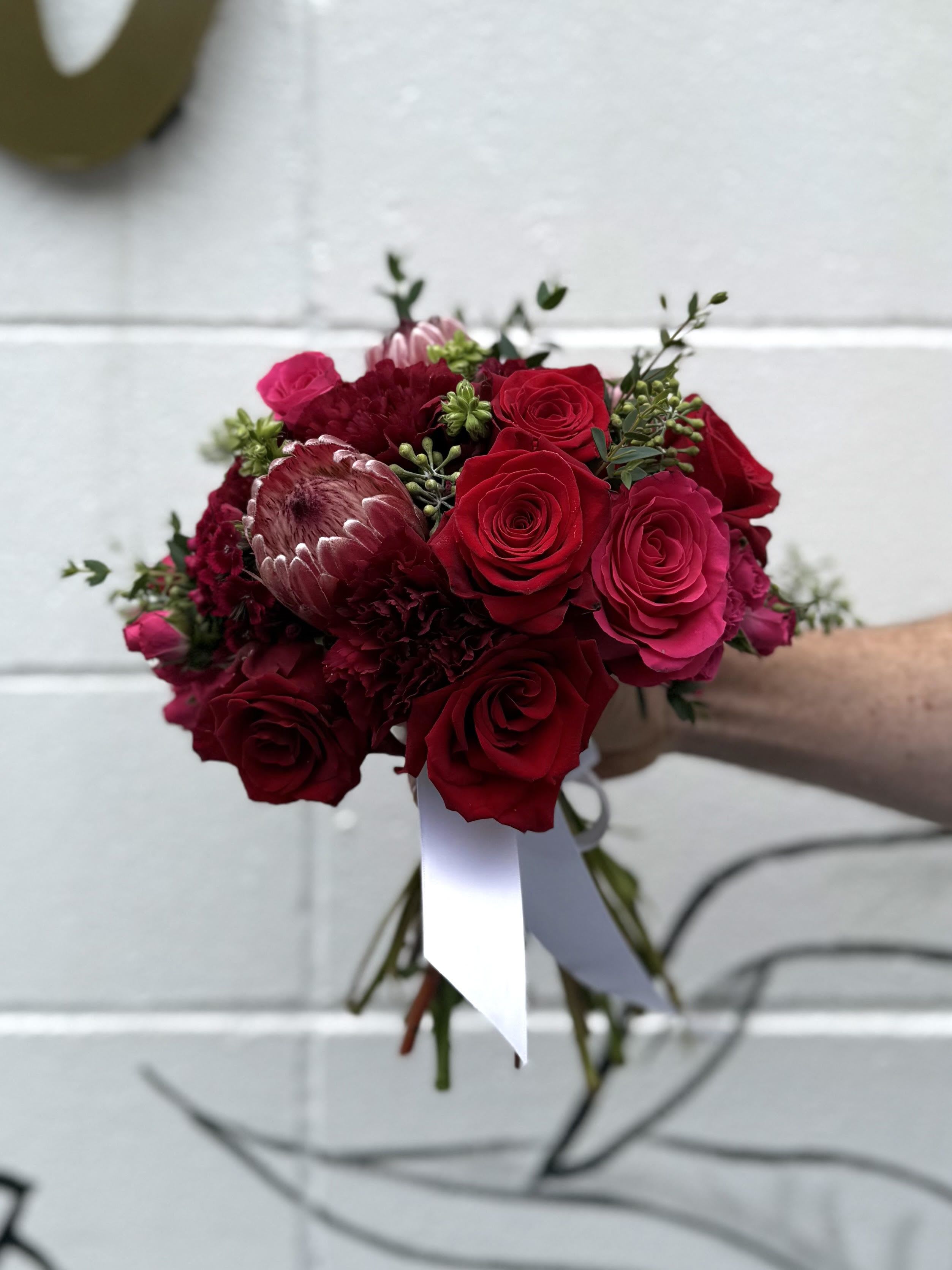 Deep Love Hand Tie - An opulent expression of passion and elegance, this bouquet showcases a lush array of deep red roses paired with rich burgundy accents. The velvety red roses symbolize love and devotion, while the burgundy hues add a touch of sophistication and depth. Perfect for romantic occasions, anniversaries, or when words aren’t enough, this arrangement speaks volumes of heartfelt emotion and timeless beauty.  Photo showcases a DELUXE sized hand tie