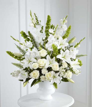 Morning Stars Arrangement or similar - The Morning Stars Arrangement is a brilliant expression of peace and soft serenity. White roses, carnations, gladiolus, stock, and Oriental lilies are accented with the bright green stems of Bells of Ireland and a gorgeous assortment of lush greens, while seated in a white designer plastic urn to create a beautiful way to honor the life of the deceased. FLOWERS MAY VARY BUT COLOR WILL REMAIN THE SAME.