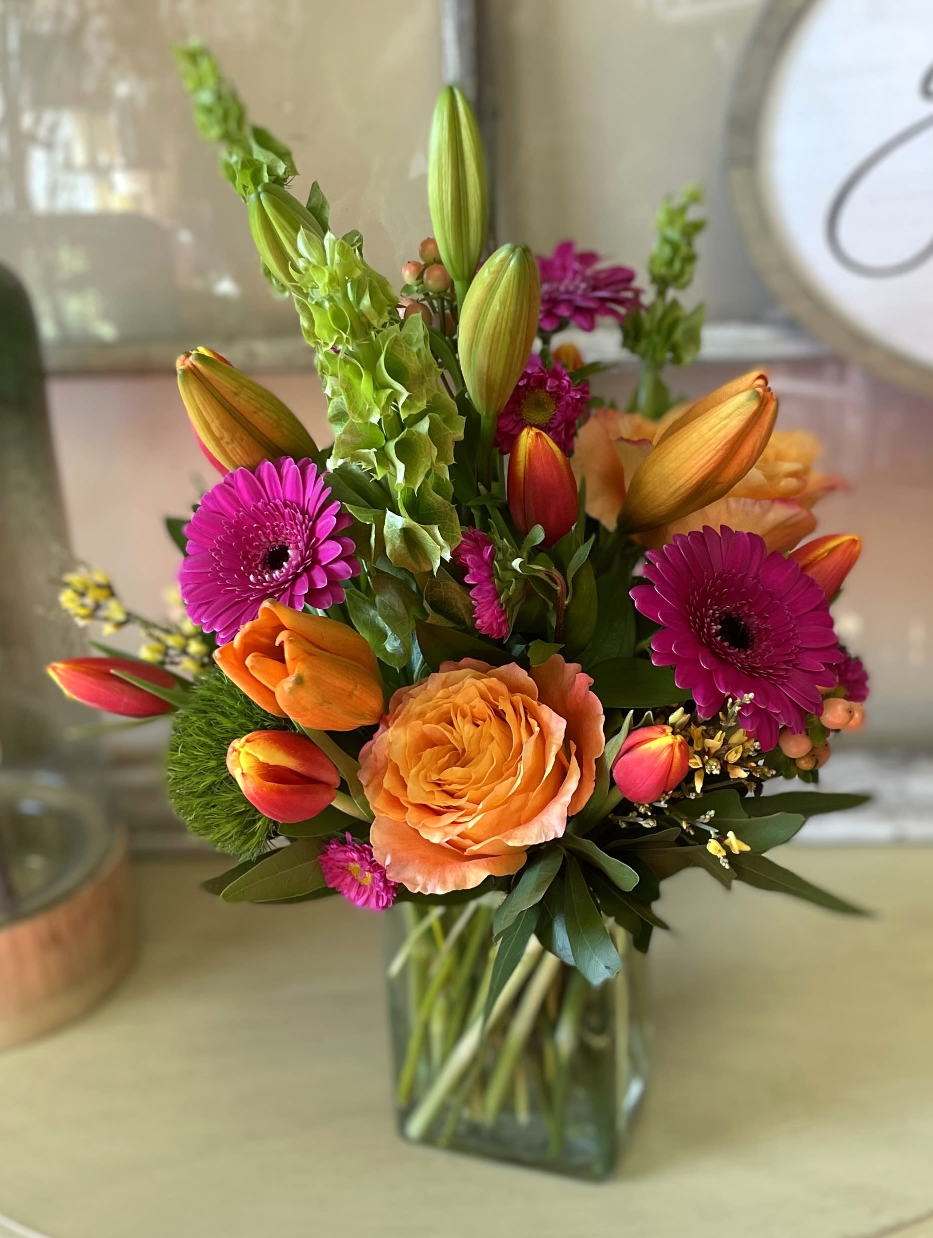 Zesty Sunrise - This vibrant flower arrangement bursts with the refreshing energy of citrus hues, featuring hot pink gerbera daisies that add a playful pop of color. The lively lime green Bells of Ireland bring a zesty, fresh touch, while the rich orange roses infuse the composition with warmth and radiance. Together, these bold blooms create a striking and cheerful display, perfect for adding a splash of brightness and energy to any space. The combination of citrus-inspired shades evokes a sense of fun, freshness, and warmth, making it an ideal choice for a lively, springtime celebration or a sunny, uplifting occasion.