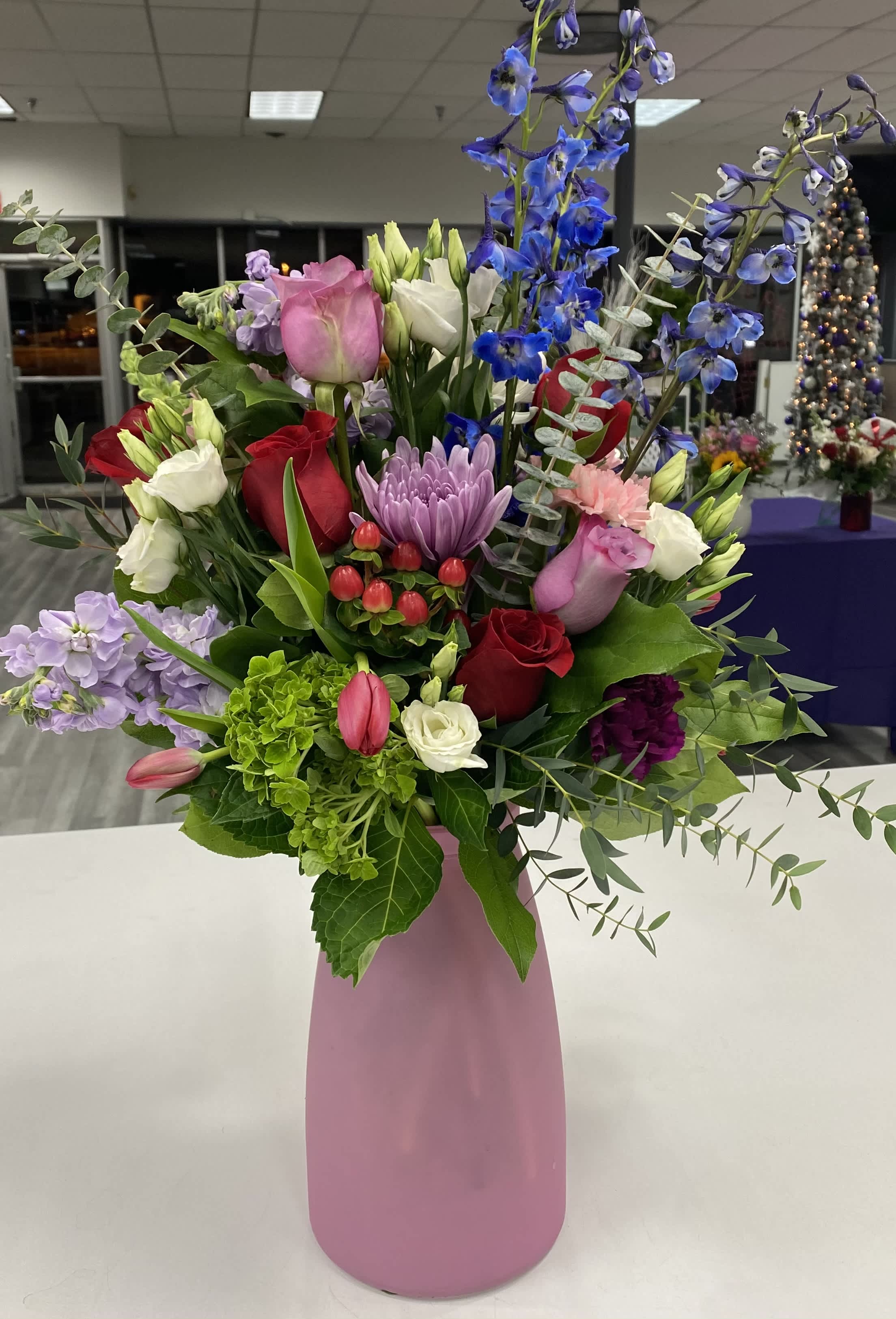 From The Heart - A tall arrangement of pinks, reds, and purples with an unexpected pop of blue. Combining classic roses with a variety of flowers for size and texture.