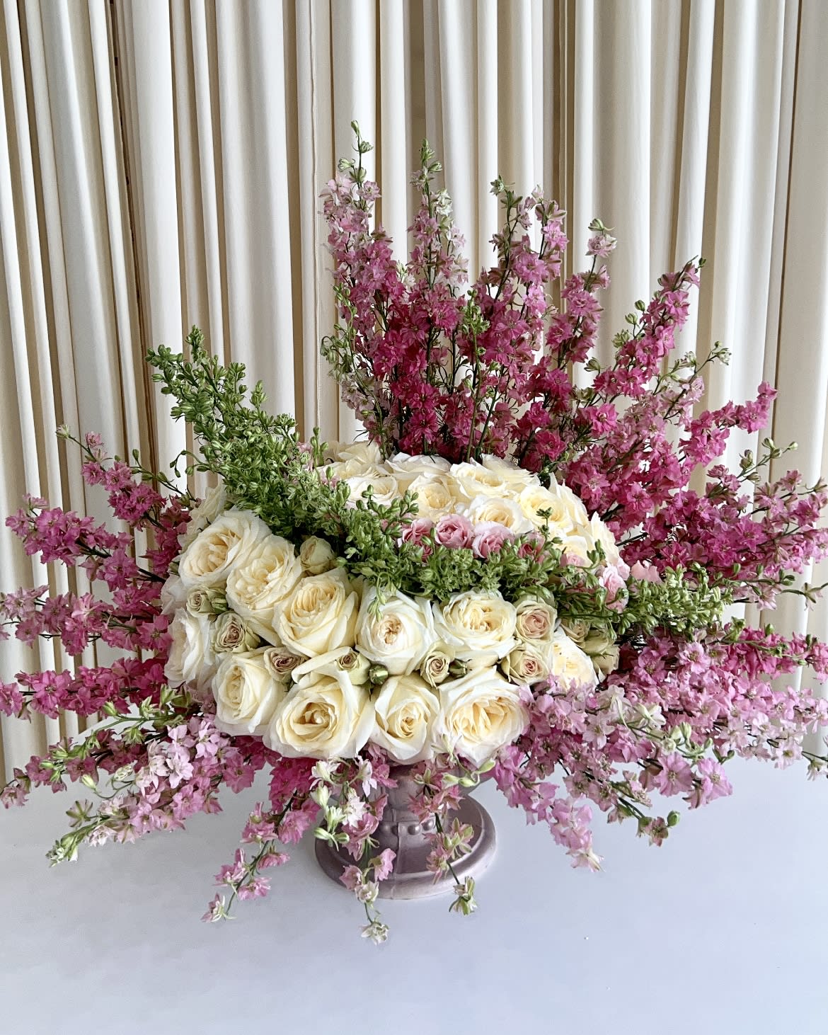 Enchanted Garden - Make it a day to remember by surprising your loved one with this elegant arrangement with white roses, baby roses and beautiful pink Larkspur flowers tied together in stunning concrete vase. This arrangement is the perfect way to put a smile on anyone's face.