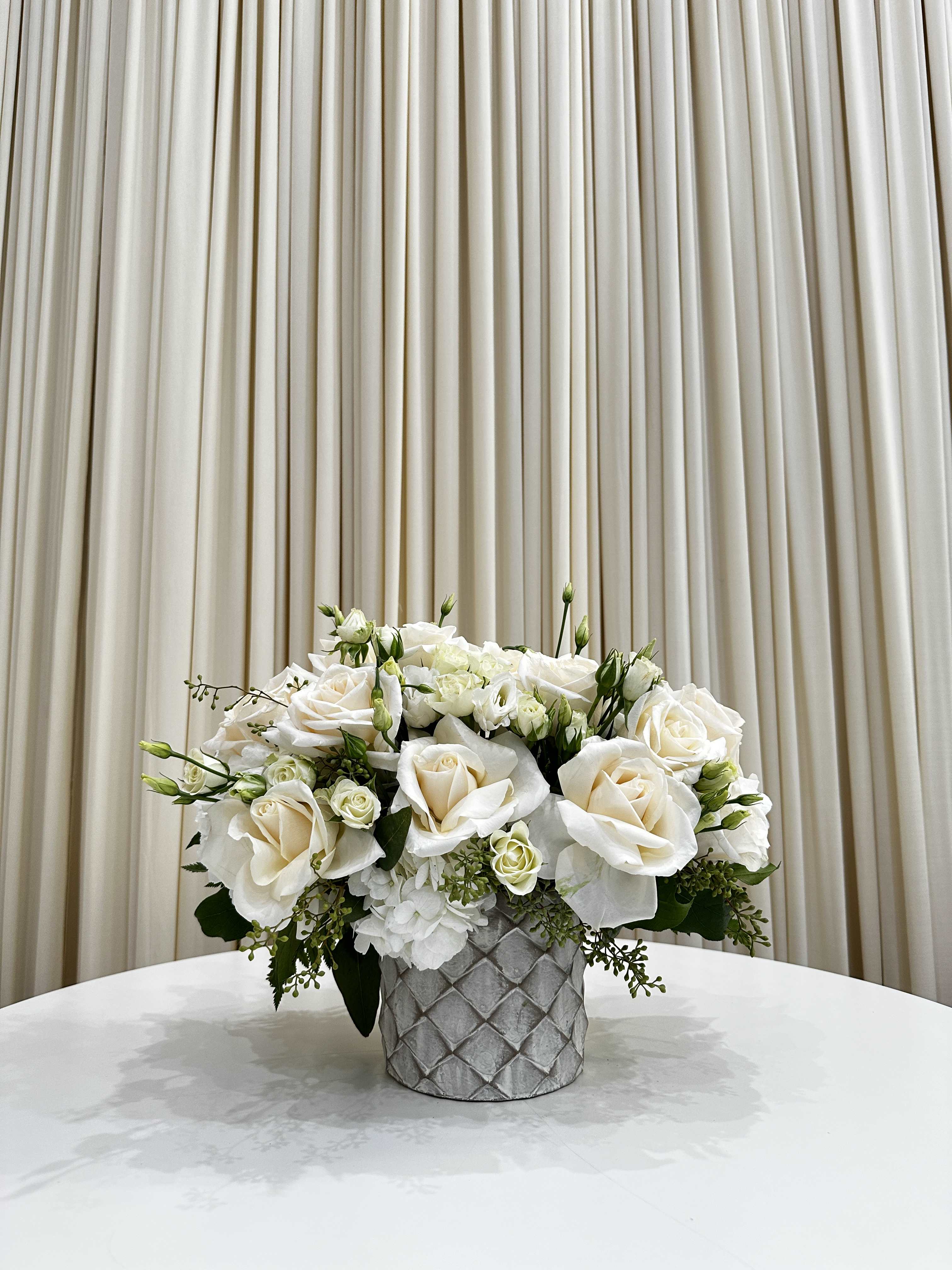 White Serenity - This elegant sympathy arrangement features a stunning white flower arrangement delicately arranged in a tasteful vase. The white flowers, symbolizing purity and innocence, create a serene and calming atmosphere, perfect for expressing condolences and sympathy during difficult times.