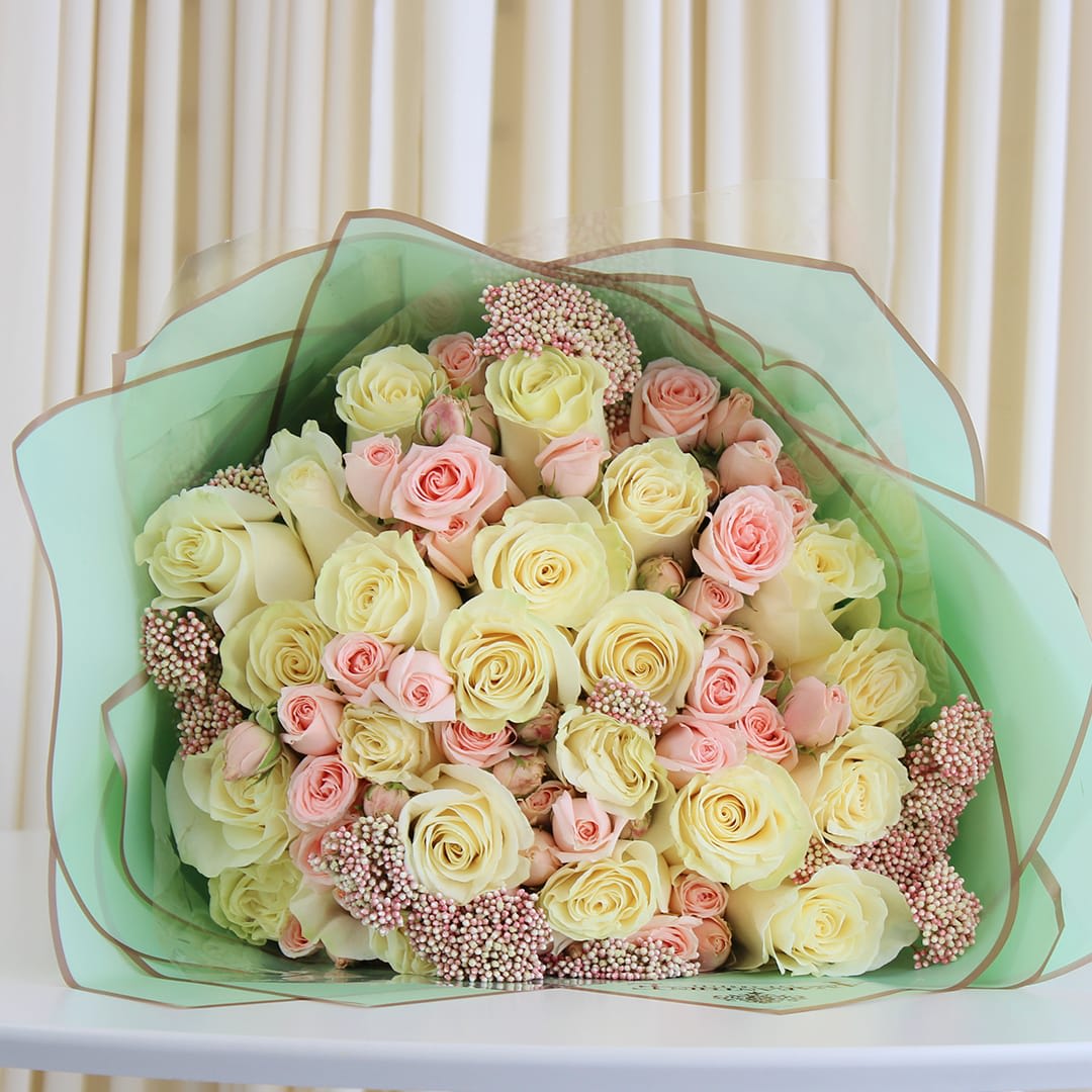 Cotton Candy Dreams - This exquisite bouquet showcases the timeless beauty of white and pink roses, delicately entwined with soft, blush-hued flowers. Nestled in a dreamy embrace of pastel-colored paper, this charming bouquet captures the essence of sugary nostalgia.  The pristine white roses symbolize purity and grace, while the blush-pink roses express admiration and appreciation. Complemented by the whimsical allure of the pink filler flowers, this bouquet exudes an air of tender affection and fond memories.  Perfect for celebrating joyous occasions, expressing heartfelt emotions, or simply brightening someone's day with its pastel splendor.