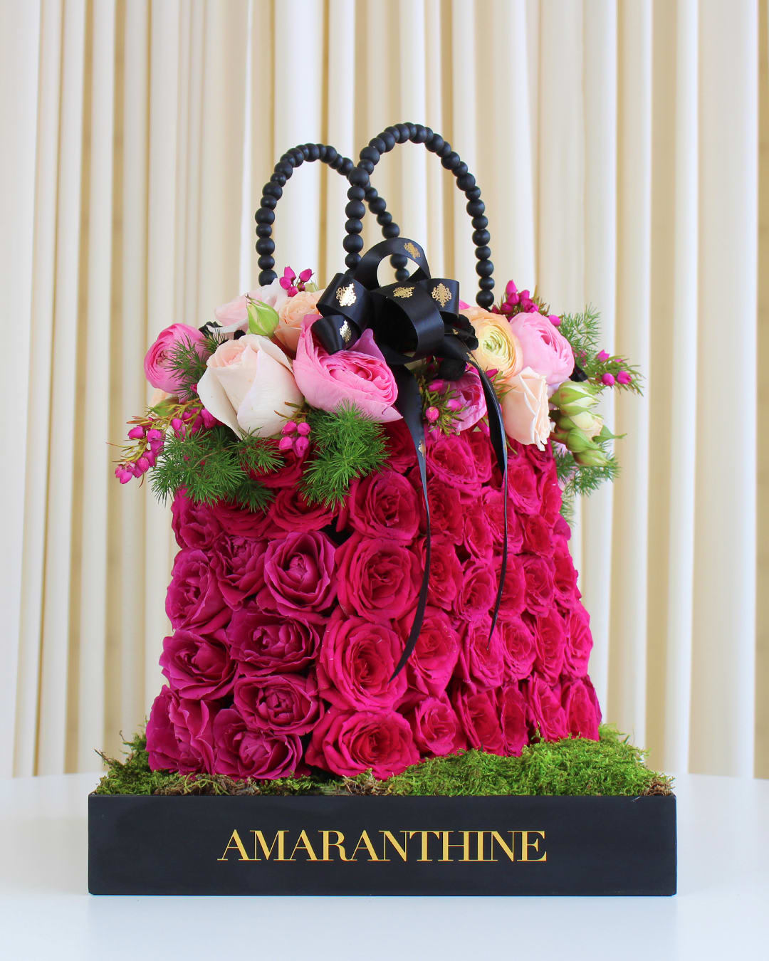 Rose and Ranunculus Purse Arrangement Rose and Ranunculus Purse Arrangement - Indulge in the sheer elegance of our "Rose and Ranunculus Purse" arrangement, a captivating display of floral artistry that redefines sophistication. Crafted with meticulous attention to detail, this stunning creation resembles a fashionable purse, adorned with brightly colored roses and delicate ranunculus flowers. Vibrant and full of life, the assortment of roses in various hues brings an explosion of color to this enchanting arrangement. Their petals exude charm, representing love, admiration, and joy. The addition of delicate ranunculus flowers adds an extra layer of finesse, embodying grace and radiant charm.