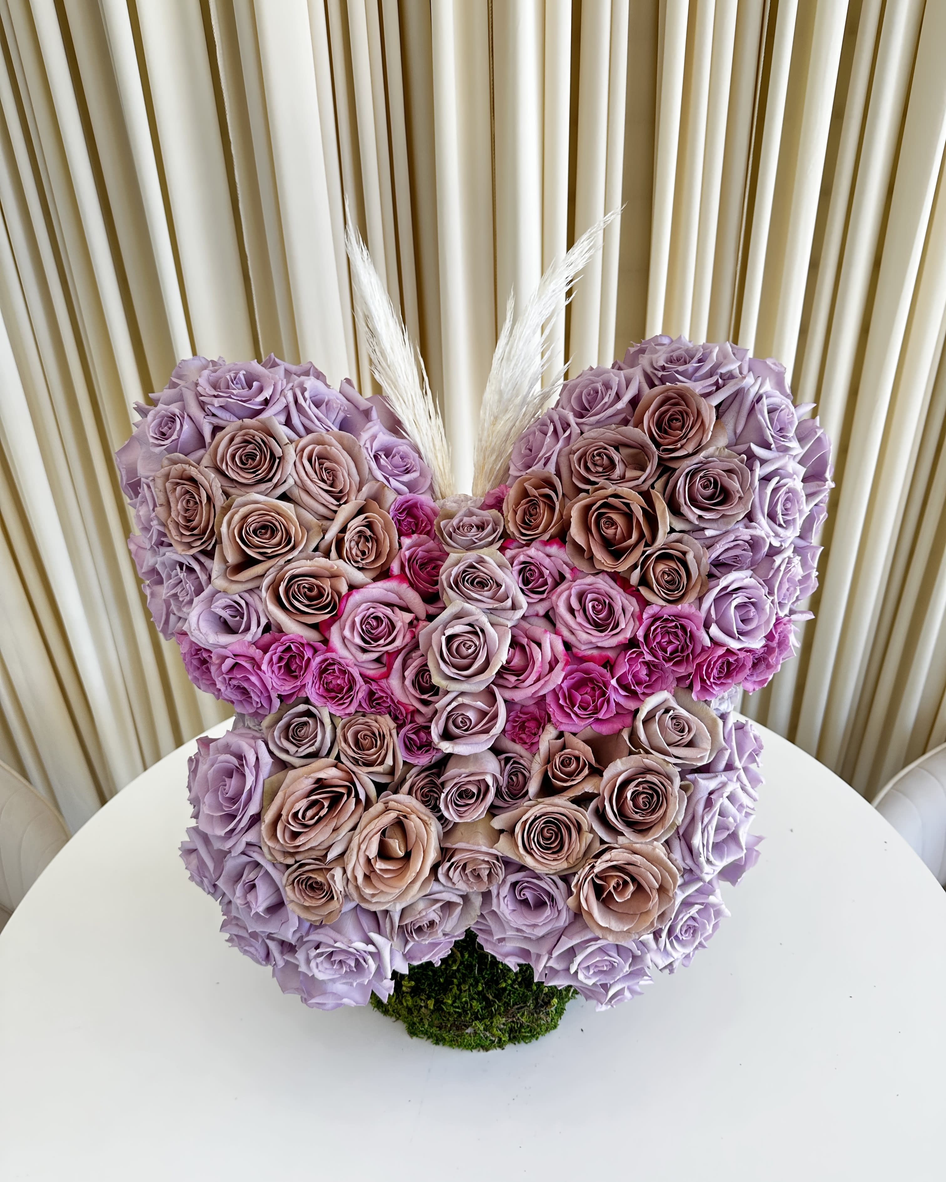 Enchanted Butterfly Blooms - Introducing our exquisite &quot;Enchanted Butterfly Blooms&quot; – a captivating floral masterpiece that combines the elegance of roses with the whimsy of nature's most enchanting creature. This stunning butterfly-shaped flower arrangement is handcrafted with a symphony of velvety purple and earthy brown roses, meticulously arranged to create a mesmerizing visual spectacle.  Each petal is carefully selected for its color and texture, ensuring a seamless transition from the delicate wings to the gracefully curved body. The blend of deep purples and earthy browns evokes a sense of both mystery and warmth, making it the perfect gift for a variety of occasions.  Whether you're looking to surprise a loved one, celebrate a special event, or simply brighten up your living space with a touch of natural artistry, our &quot;Enchanted Butterfly Blooms&quot; is the ideal choice. This unique floral creation not only radiates the beauty of nature but also symbolizes transformation, making it a meaningful addition to any room or a heartfelt gesture to convey your sentiments.  