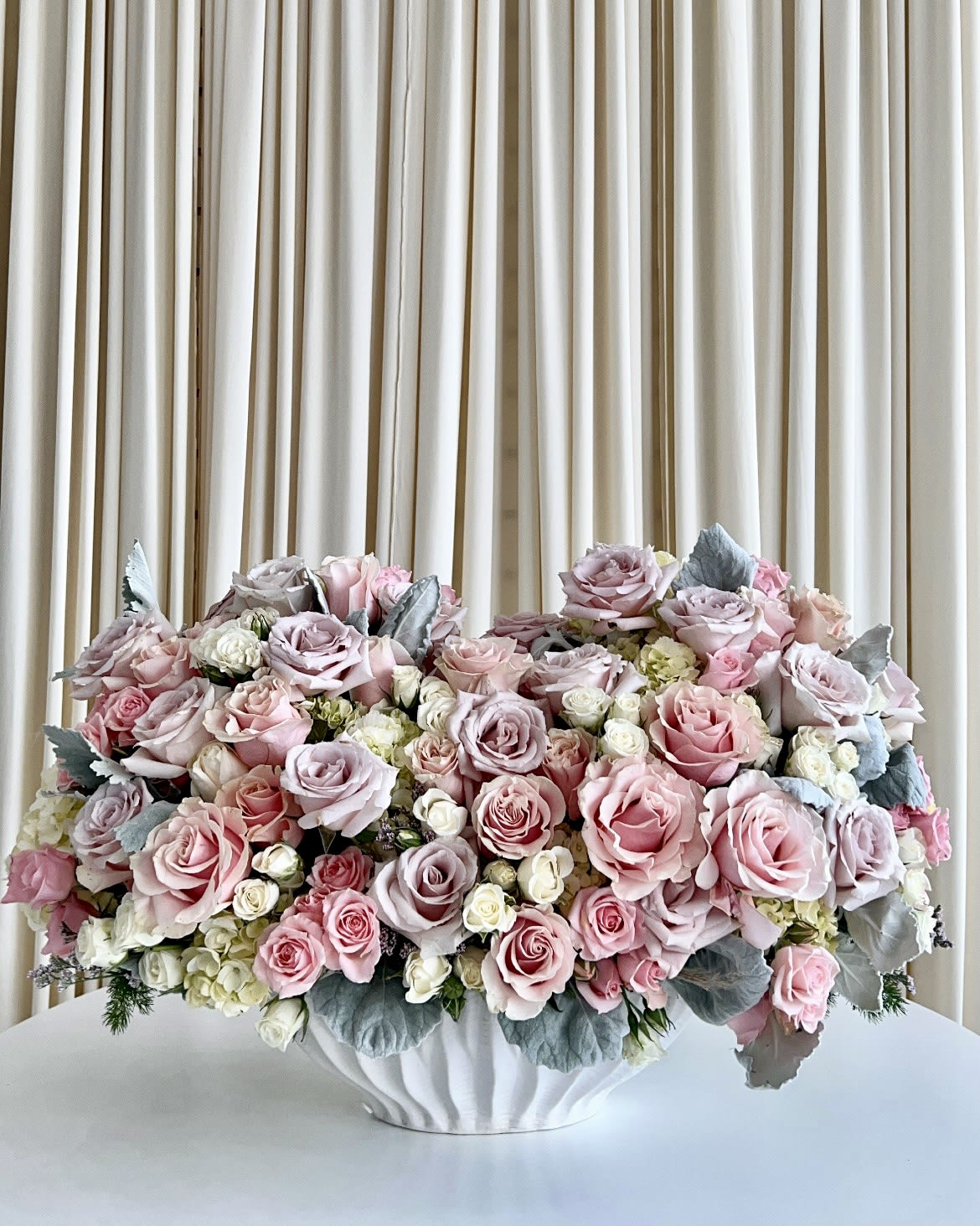 Pastel Elegance Blossom - Introducing our exquisite &quot;Pastel Elegance Blossom&quot; – a stunning floral arrangement that embodies the delicate beauty of nature. This enchanting creation is designed to infuse your space with a sense of serenity and grace.  Nestled in a pristine white vase, this arrangement showcases a harmonious blend of pastel-colored florals that evoke a sense of tranquility and refinement. Soft shades of pink and purple petals come together in perfect symphony, creating a soothing visual experience that captivates the heart.  Each bloom in the &quot;Pastel Elegance Blossom&quot; has been hand-selected for its freshness and elegance, ensuring that your arrangement will radiate its natural splendor for days on end. Whether adorning your home, office, or as a heartfelt gift, this arrangement serves as a testament to your impeccable taste and appreciation for life's simple, beautiful moments.