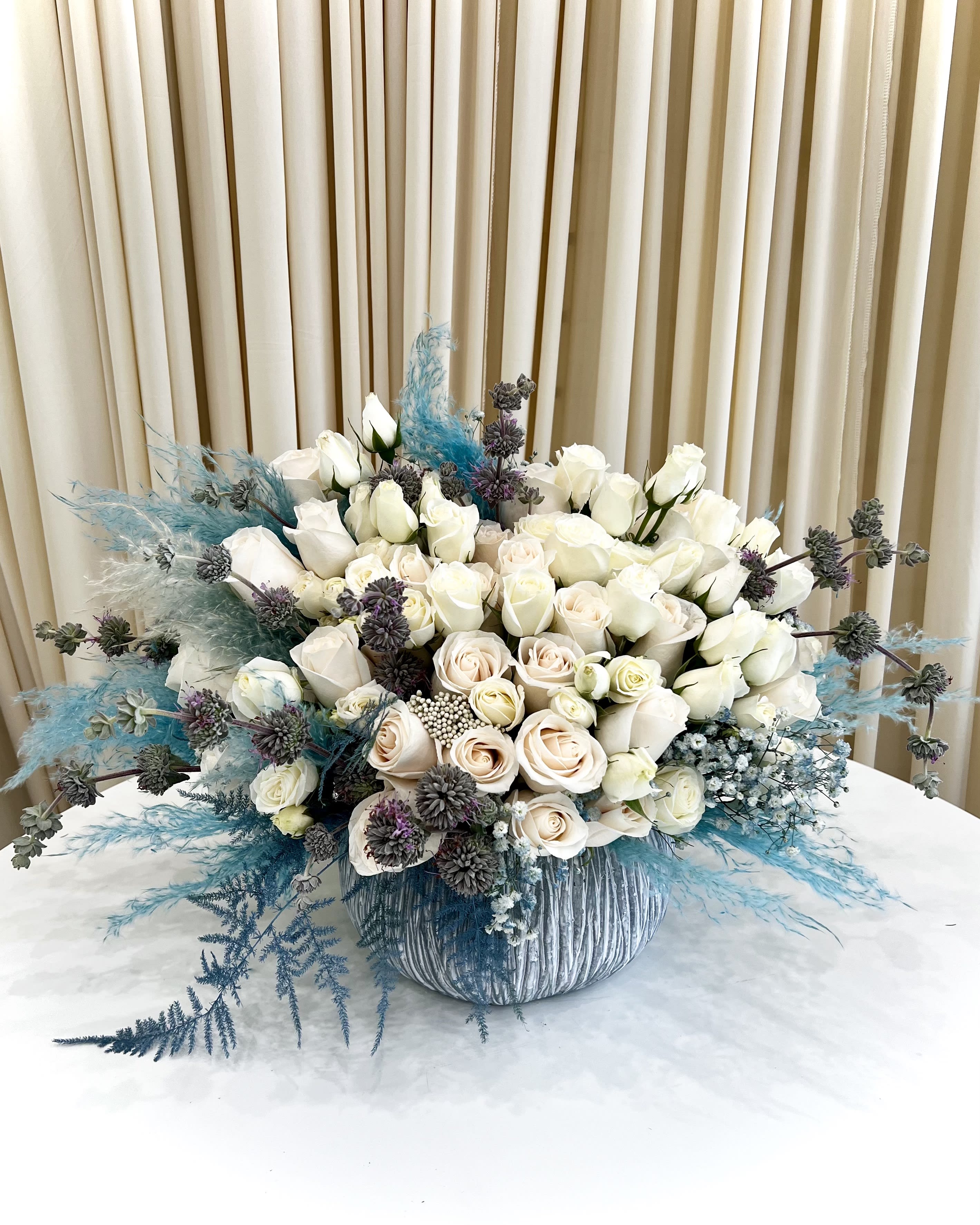Tranquil Teal Elegance - Elevate your space with our enchanting &quot;Tranquil Teal Elegance.&quot; This stunning floral masterpiece combines the timeless purity of white blossoms with the soothing allure of teal accents, creating a harmonious blend that's perfect for any occasion.  In this exquisite arrangement, pristine white roses take center stage, symbolizing purity, love, and elegance. The teal florals, carefully interwoven among the whites, add a touch of serenity and uniqueness to the bouquet. Teal represents calmness and tranquility, making this arrangement ideal for both celebratory moments and moments of reflection.  Each bloom is expertly hand-selected and arranged by our skilled florists to ensure a captivating balance of colors and shapes. The &quot;Tranquil Teal Elegance&quot; is presented in a chic vase, adding a touch of sophistication to any setting.  Whether you're celebrating a special occasion, expressing your deepest emotions, or simply brightening up your home or office, this arrangement is the embodiment of refined beauty and tranquility. It's a thoughtful gift that will be cherished by your loved ones or a captivating addition to your own decor.