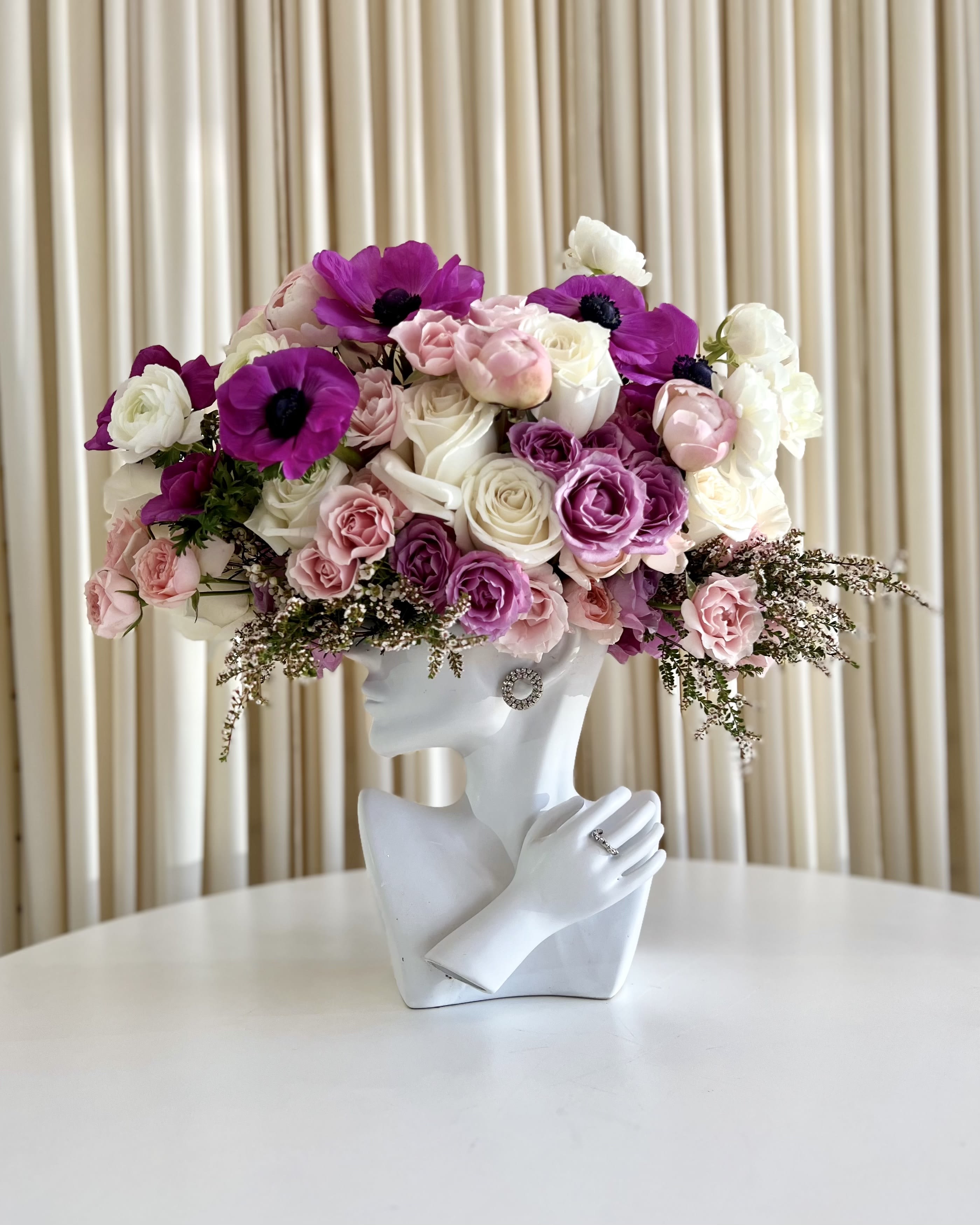 Ethereal Goddess - Embrace the enchanting beauty of the &quot;Ethereal Goddess&quot; Sculpture Vase, a mesmerizing blend of art and nature. This exquisite vase showcases a stunning women head sculpture, exuding elegance and grace, crowned with a resplendent arrangement of purple, pink, and white flowers. The delicate purple anemone's add a beautiful dazzle to this captivating masterpiece, making it a truly unique and artistic centerpiece for any space. Elevate your décor with this ethereal fusion of feminine allure and the timeless charm of floral artistry.