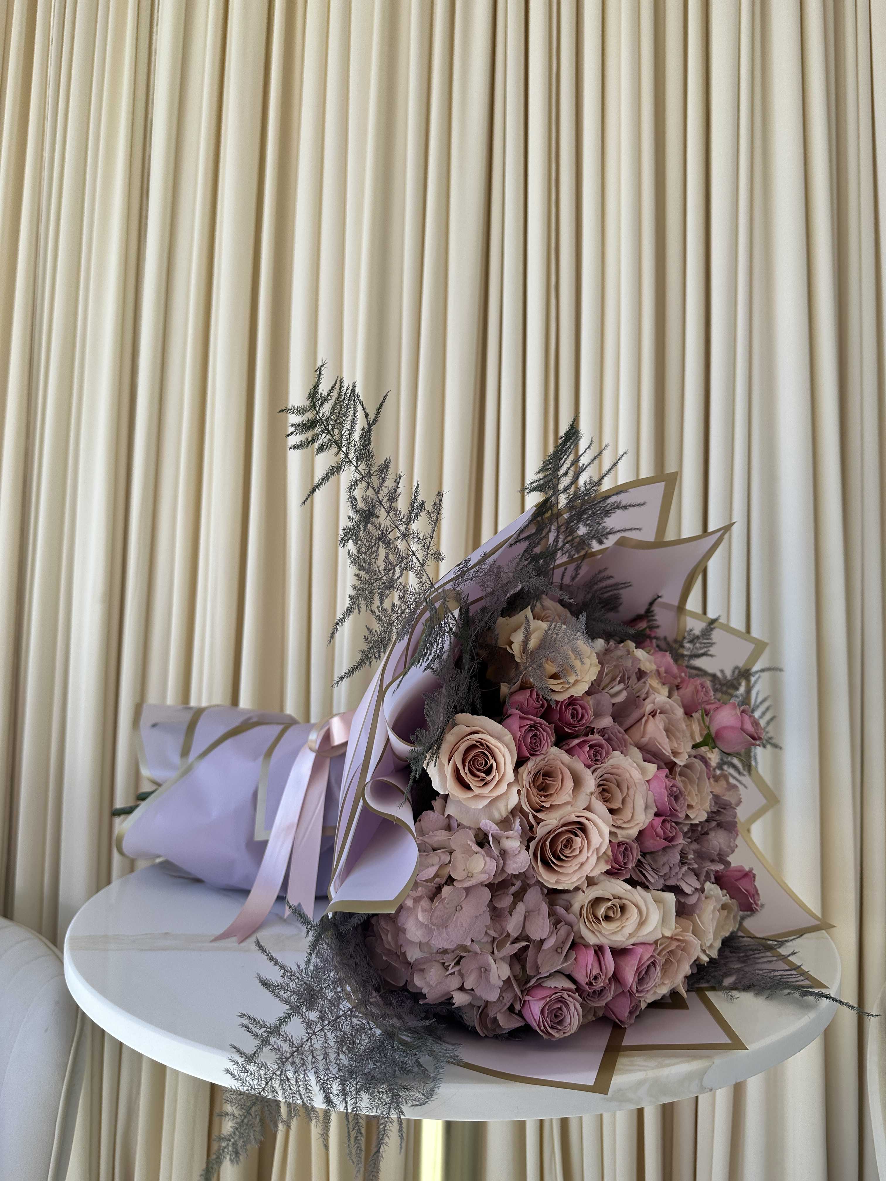 Enchanting Twilight - This enchanting bouquet evokes the beauty of twilight with its captivating blend of colors. Lush hydrangeas in jewel tones of purple and sapphire create a mesmerizing base, while soft blush roses add a touch of ethereal elegance. Delicate purple baby roses complete the arrangement, bringing a hint of playfulness and innocence.