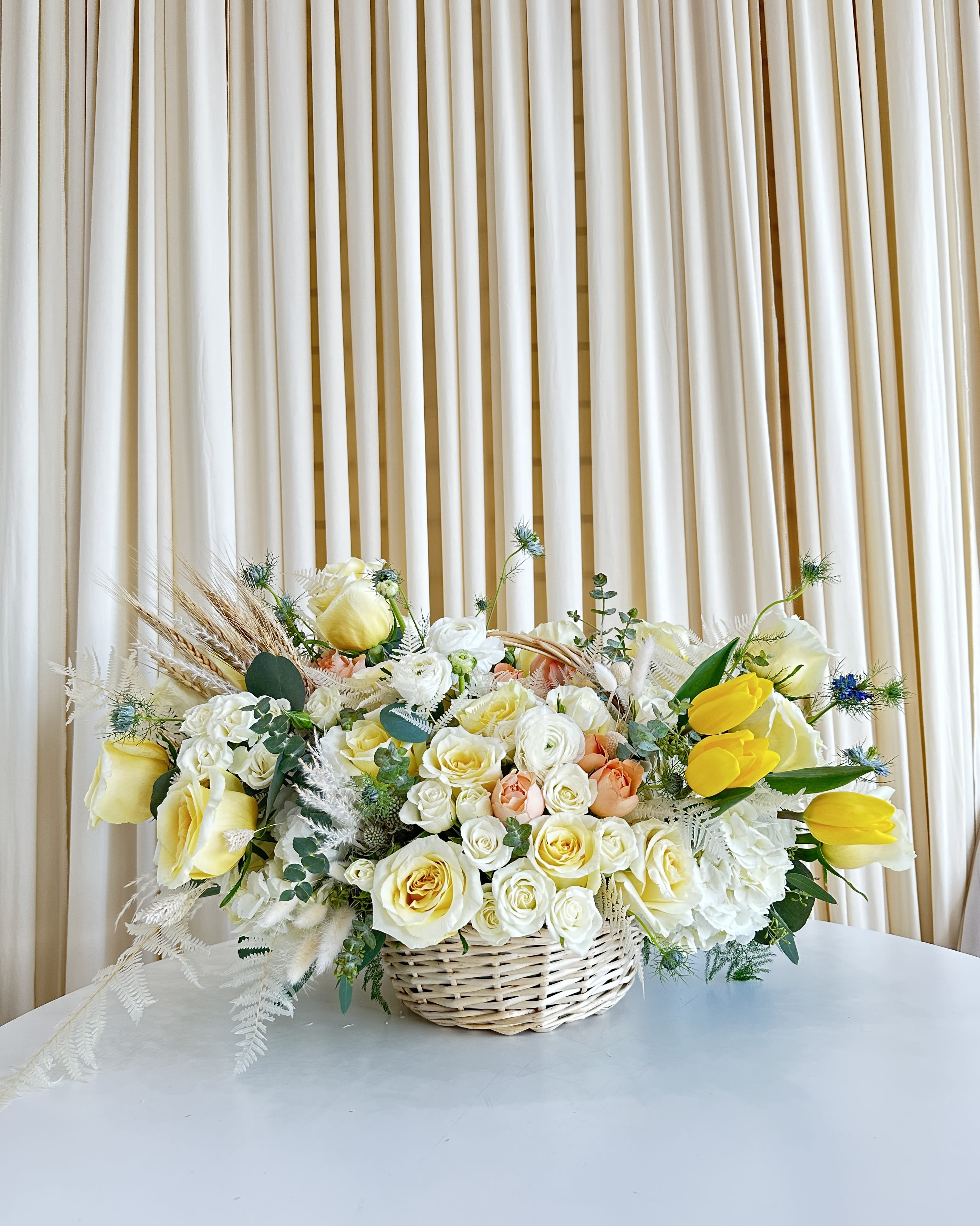 Bliss in a Basket - Immerse yourself in the warmth of our floral basket, a captivating symphony of white, yellow, and peach florals that radiate pure bliss. Nestled in a charming basket, this arrangement is a celebration of nature's vibrant hues and delicate fragrances. The harmonious blend of colors invites the spirit of joy and positivity into any space. Perfect for brightening someone's day or adding a touch of sunshine to your own surroundings, &quot;Bliss in a Basket&quot; captures the essence of nature's beauty in every petal. Embrace the radiance and elegance of this enchanting arrangement – a true testament to the artistry of blossoms.