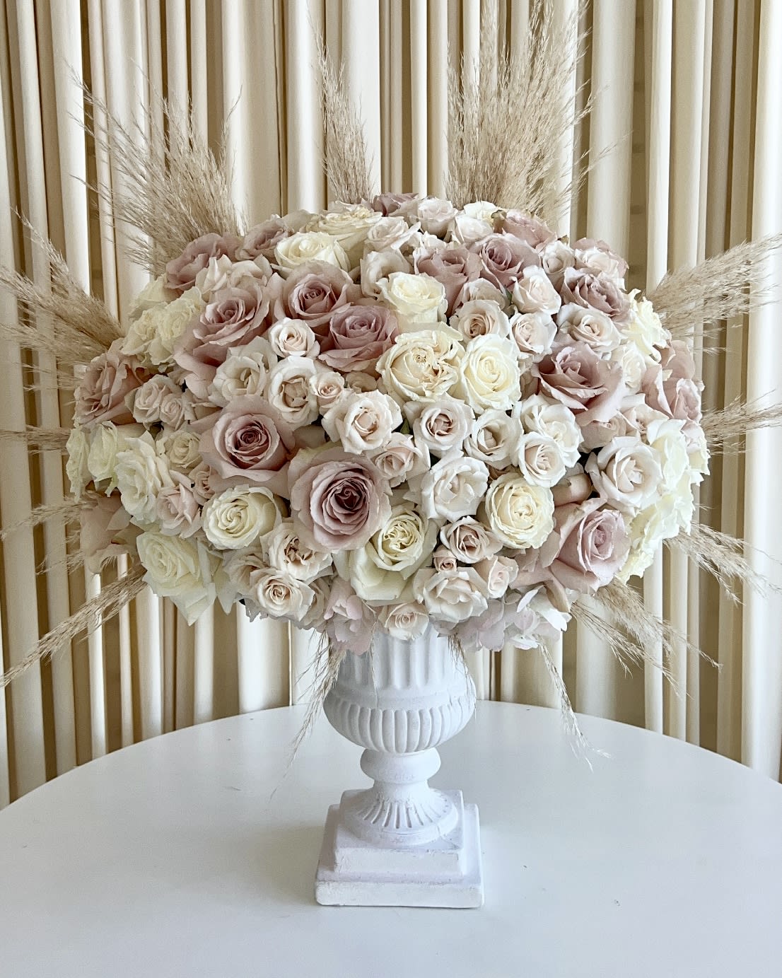 Serene Whispers Serene Whispers - Indulge in the gentle beauty of our "Serene Whispers" flower arrangement, thoughtfully designed to captivate your senses. Delicate neutral-colored roses and hydrangeas come together in perfect harmony within a stunning white pedestal vase, exuding an air of elegance and tranquility. To add a whimsical touch, we've incorporated a hint of pampas, gently swaying like whispers of serenity. Elevate your space with this exquisite masterpiece, a captivating blend of grace and charm that will leave you enchanted.