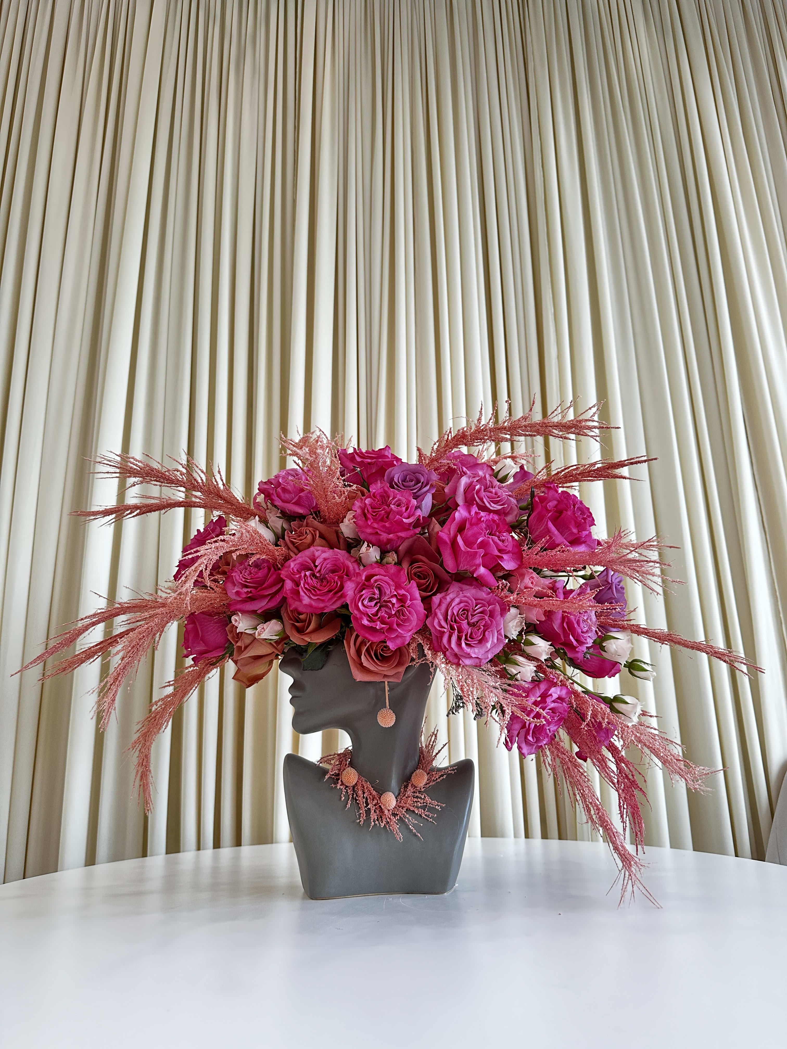 Vibrant Splendor - Experience the allure of &quot;Vibrant Splendor,&quot; a head-shaped flower arrangement that embraces the spirit of boldness and beauty. This stunning medley of hot pink and fiery orange roses comes together in a captivating display that will leave you enchanted.  Elegantly adorned with delicate feathers for a touch of whimsy, this one-of-a-kind creation combines sophistication with a dash of playfulness, making it a stunning arrangement to gift to someone.  Indulge in the radiant charm of hot pink and fiery orange hues, as &quot;Vibrant Splendor&quot; brings warmth and vivacity to any space. This head-shaped arrangement is a true embodiment of floral artistry, expertly crafted to reflect the brilliance of nature's colors.  Add a touch of drama and flair to your surroundings with &quot;Vibrant Splendor,&quot; an exceptional masterpiece that celebrates the exuberance of roses and the whimsical charm of feathers. Elevate your floral experience with this head-turning arrangement that captures the essence of vibrancy and splendor.