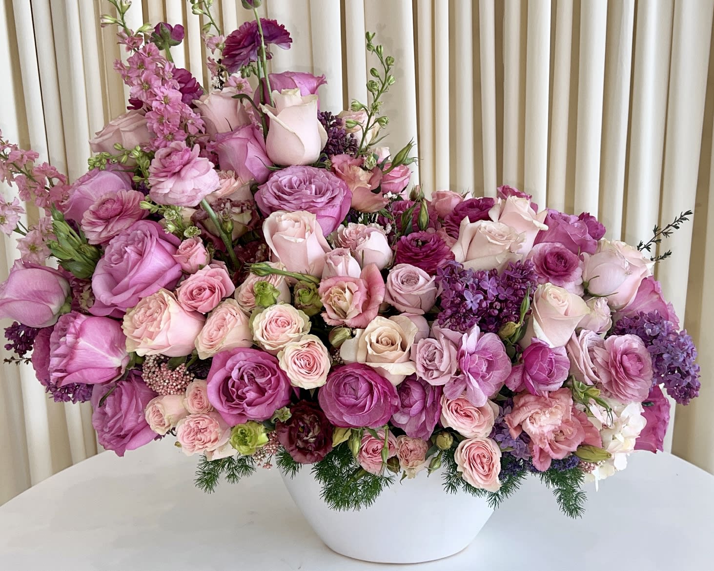 Enchanting Harmony Enchanting Harmony - Experience the allure of "Enchanting Harmony," a mesmerizing flower arrangement that captures the essence of elegance and beauty. Radiating with shades of purple and pink, this exquisite bouquet features a delightful ensemble of roses, ranunculus, lisianthus, lilacs, and perennials, carefully curated to create a symphony of colors and textures. Nestled in a pristine white vase, these blooms harmoniously blend together to form a breathtaking display that is both captivating and enchanting. The soft hues and graceful blooms evoke a sense of tranquility, making it a perfect addition to any space or a thoughtful gift to express your love and appreciation. Indulge in the splendor of nature's finest as "Enchanting Harmony" becomes the focal point of admiration at weddings, celebrations, or simply brightens your everyday moments. Embrace the magic of this floral creation and let it infuse your surroundings with an aura of sophistication and joy. Bring the charm of purple and pink florals into your life with "Enchanting Harmony" and elevate your floral experience to new heights. Witness the magical fusion of colors and fragrances that are sure to leave a lasting impression on all who behold this stunning arrangement.
