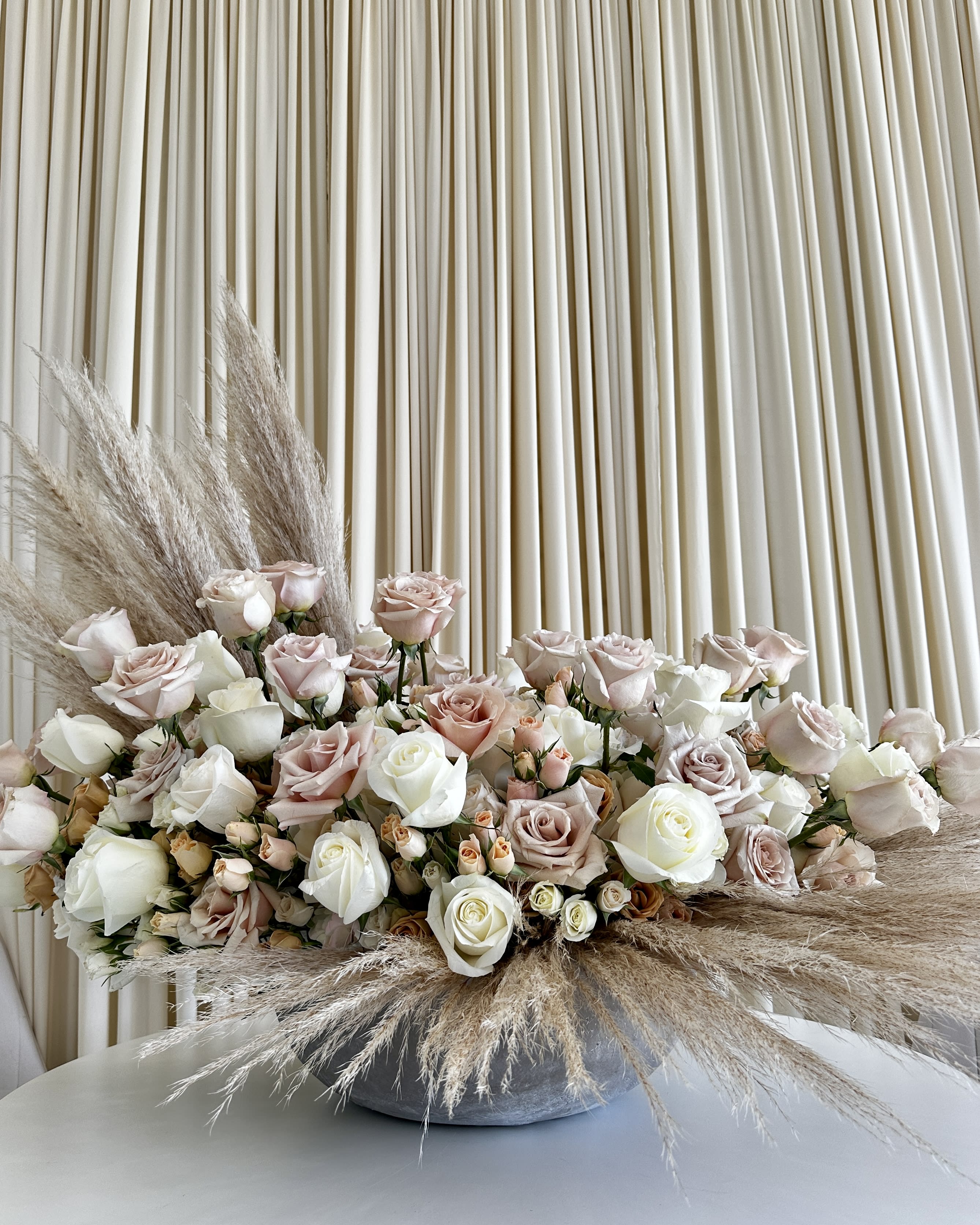 Elegant Harmony: Roses &amp; Pampas Bliss - Introducing our &quot;Elegant Harmony: Roses &amp; Pampas Bliss&quot; flower arrangement – a masterpiece that captures the timeless beauty of neutral-colored roses and the ethereal grace of pampas grass. This exquisite floral creation is designed to elevate any space with its sophisticated charm and gentle allure.  Each bouquet is meticulously crafted by our skilled florists, blending the soft, romantic hues of neutral roses with the delicate, feathery elegance of pampas grass. The result is a harmonious symphony of nature's finest elements, bound together in a stunning display of artistry and style.  Whether you're seeking the perfect gift to convey your sentiments or want to adorn your own living space with a touch of natural elegance, our &quot;Elegant Harmony: Roses &amp; Pampas Bliss&quot; arrangement is the ideal choice. It's versatile enough to complement any décor, making it a wonderful addition to weddings, special occasions, or simply to brighten your everyday life.  Indulge in the soothing aesthetics of this flower arrangement, designed to evoke serenity and tranquility. Grace your surroundings with the timeless beauty of neutral-colored roses and the gentle sway of pampas grass, and experience the enchantment of &quot;Elegant Harmony&quot; today.