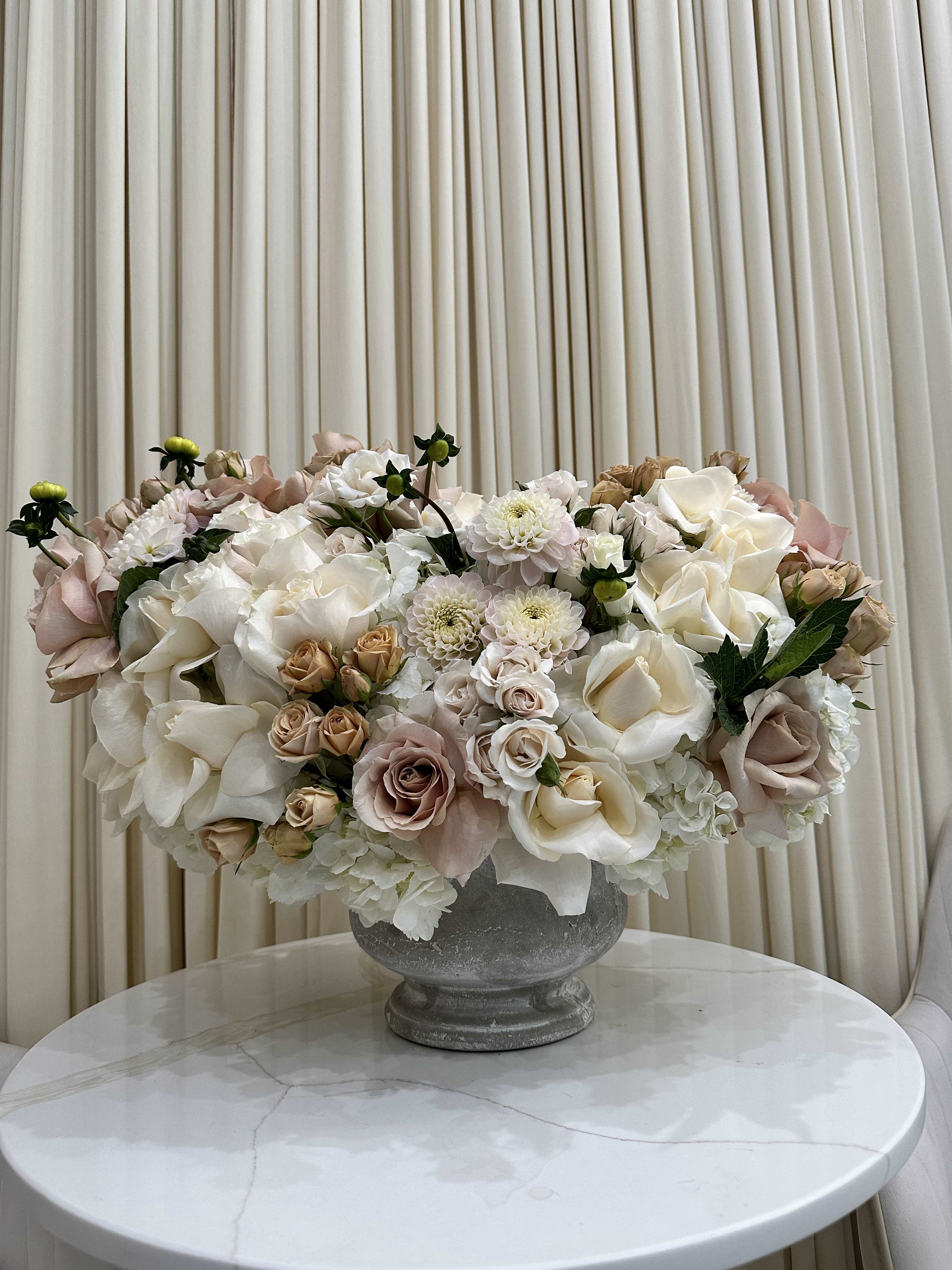 Blushing Abundance - This breathtaking arrangement is overflowing with vibrant blooms, perfect for celebrating a special occasion or simply brightening someone's day. Luscious pink, and white dahlias mingle with delicate roses and hydrangeas, creating a tapestry of color and texture that is sure to impress.
