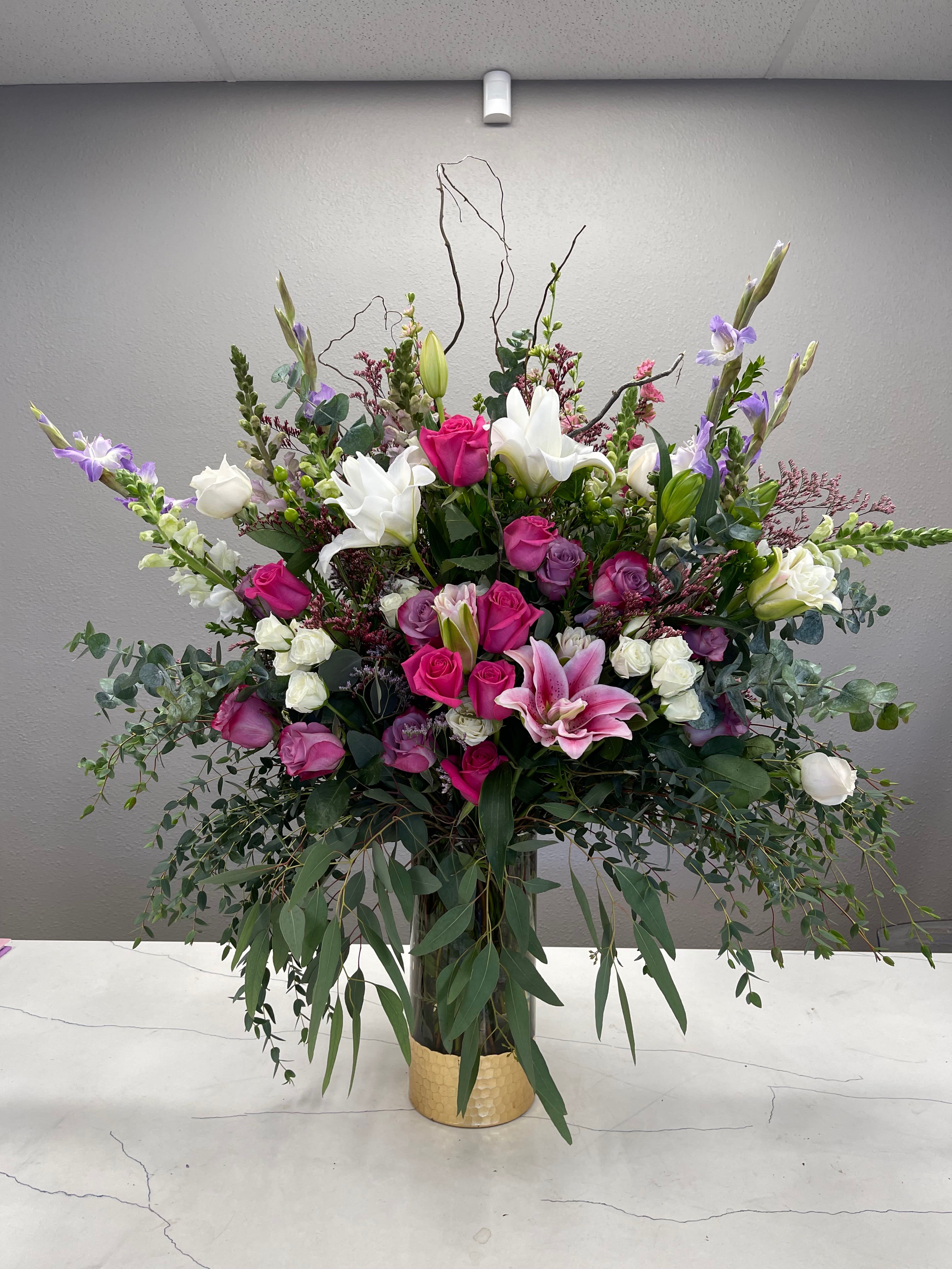 DREAMLAND - A COLORFUL SELECTION OF BLOSSOMING BUDS IN A CLEAR AND GOLD VASE.