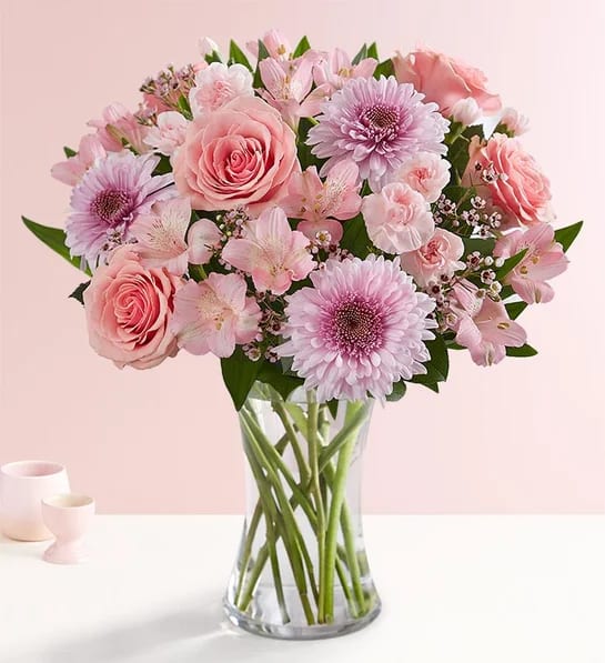 Budding Romance - A delightful medley of blooms, this arrangement features soft pink roses, charming alstroemeria, and sweet carnations, beautifully complemented by the delicate allure of lavender mums. Bursting with gentle hues and textures, it’s a perfect blend of elegance and cheer, crafted to brighten any space and bring joy to every moment.  Description: Pink roses, pink carnations, pink alstro, Lavender mums, baby's breath