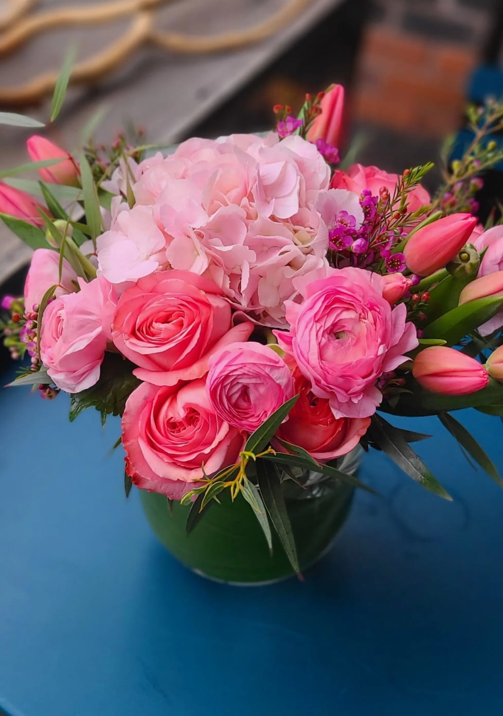 Vivienne Vivienne - A mix of vibrant pink roses,tulips,ranunculus with a variety of greens in a clear vase