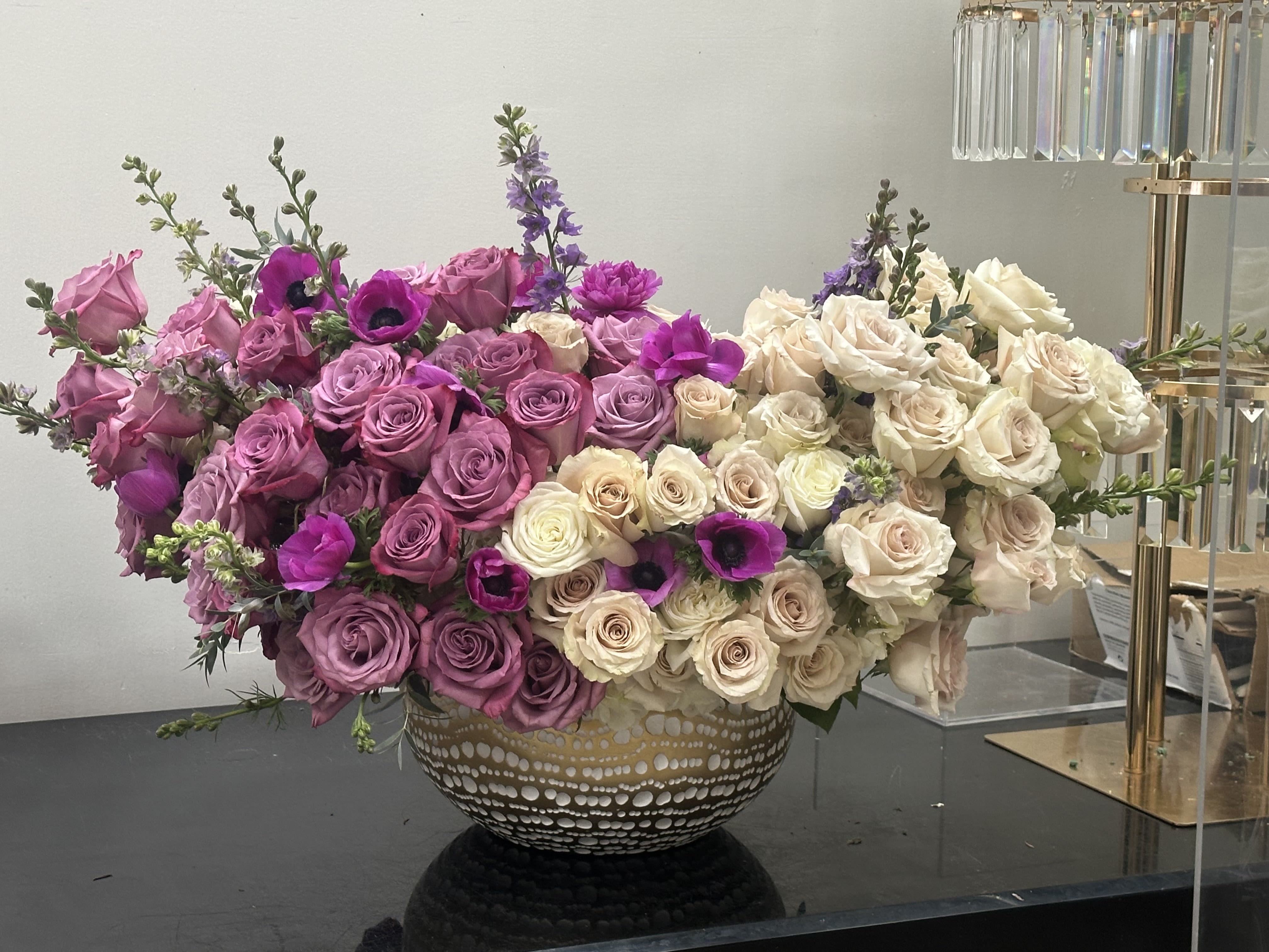 Viola Melody Viola Melody - The blending of hues from different shades of vibrant purples fading into soft ivory white pallet. Composition is full of lush purple ivory white roses touches of purple anemone and delphinium peeking out for that purple melody of blooms. Resting in a muted gold vase compliments the color pallet of the blooms. Some florals are seasonal, if particular flower will not be available due to season, we will substitute for similar flower, composition, color pallet and value of the arrangements as closely as possible. All effort to create a floral arrangement as close to the photo shown, the actual arrangement may vary slightly in its appearance from the photo shown. If you have any questions about your order, we welcome you to call us in or email